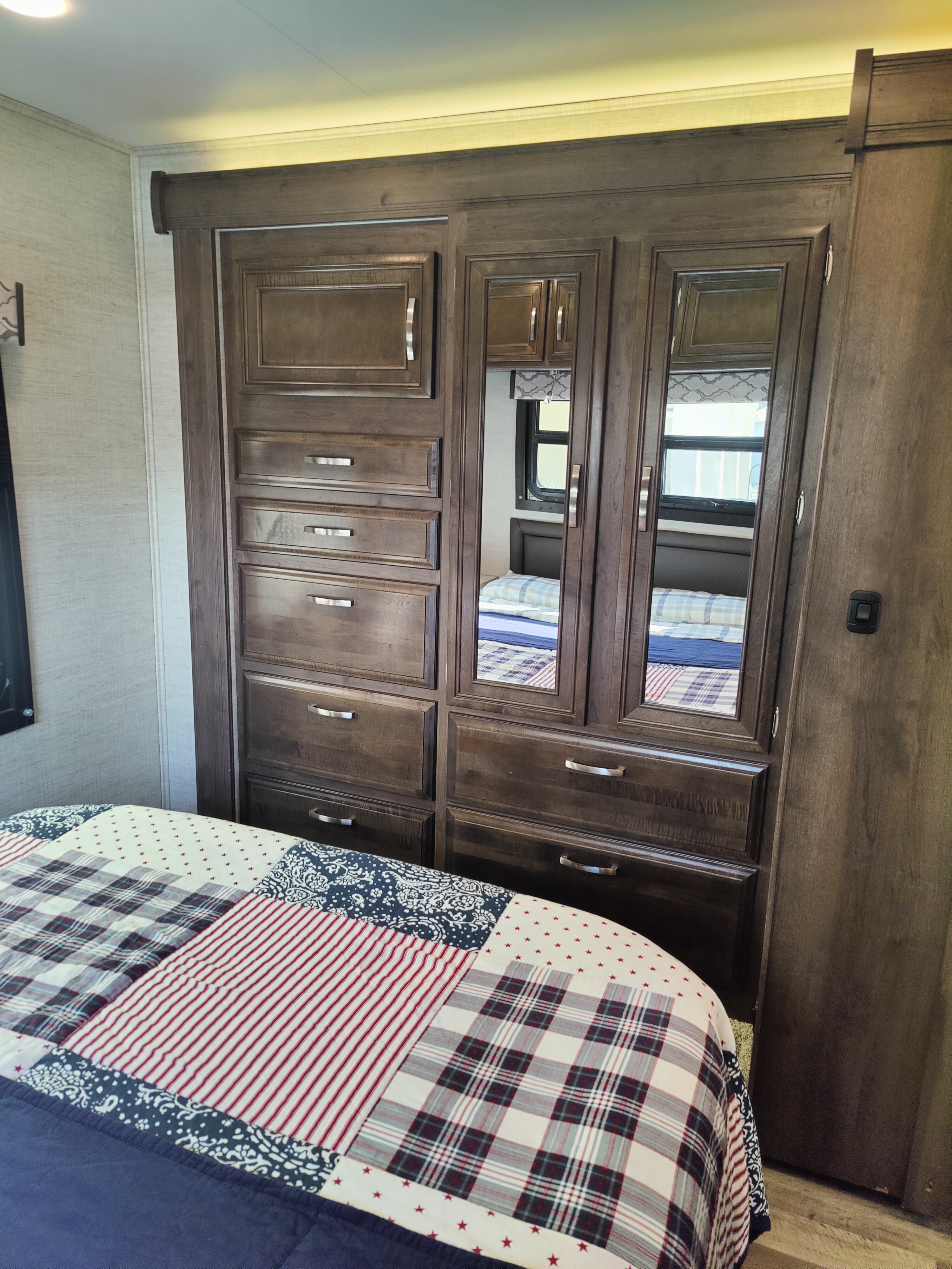 RV rental bedroom: Compact wood wardrobe with mirrored doors, drawers, and patriotic quilt. Space-saving RV storage.. Jayco Redhawk 2021
