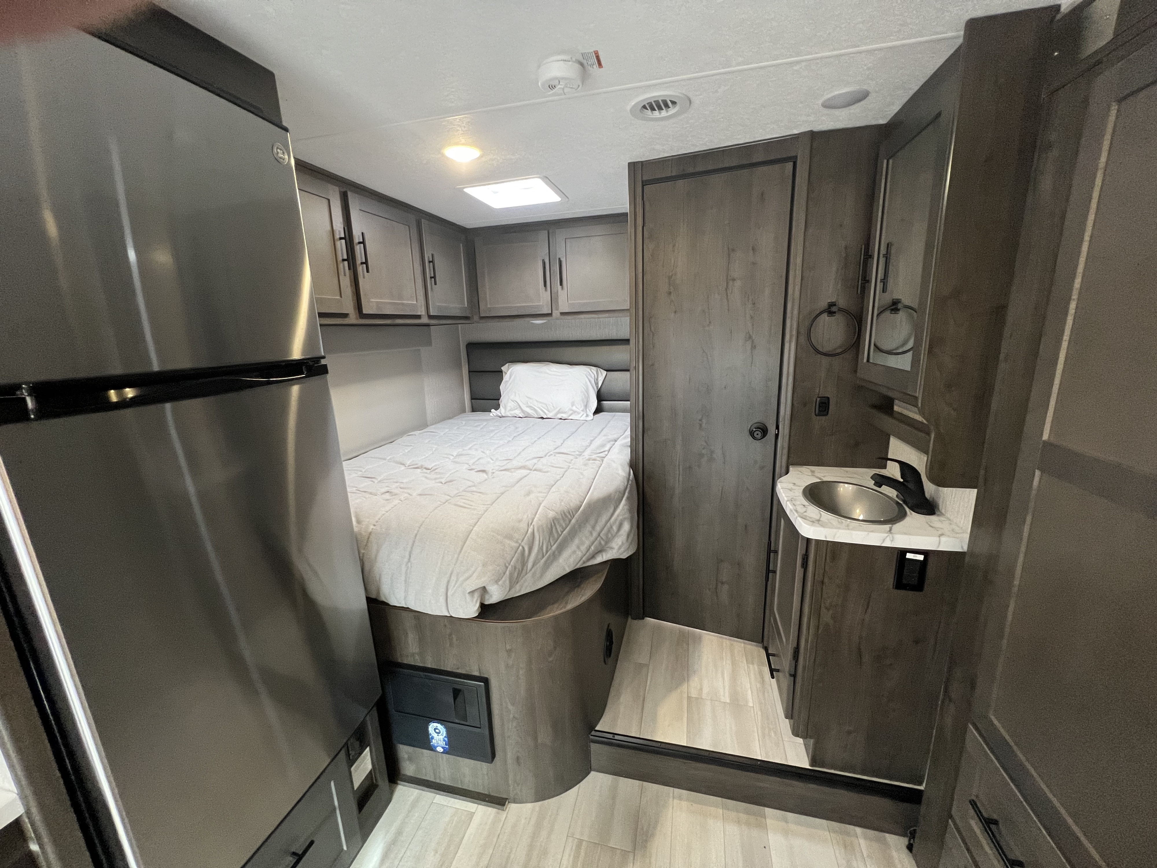 Cozy RV rental interior featuring a bedroom with bed, stainless fridge, and a compact bathroom sink area.. Forest River Coachman Prism 2150CB 2023