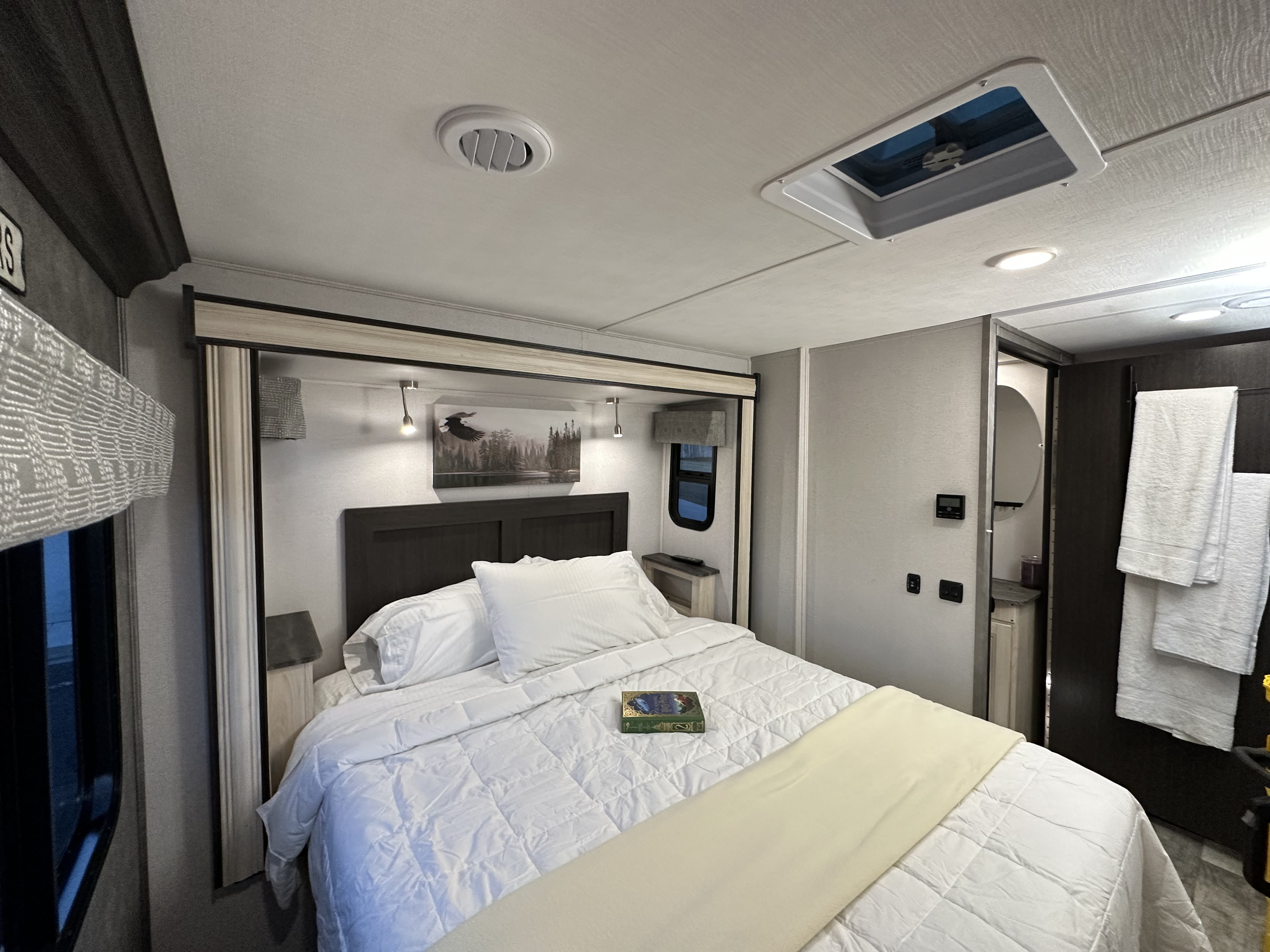 RV rental bedroom: a bright space with a queen bed, white bedding, wall art, and practical RV amenities. Bathroom entrance to the right.. Forest River Sunseeker 2023