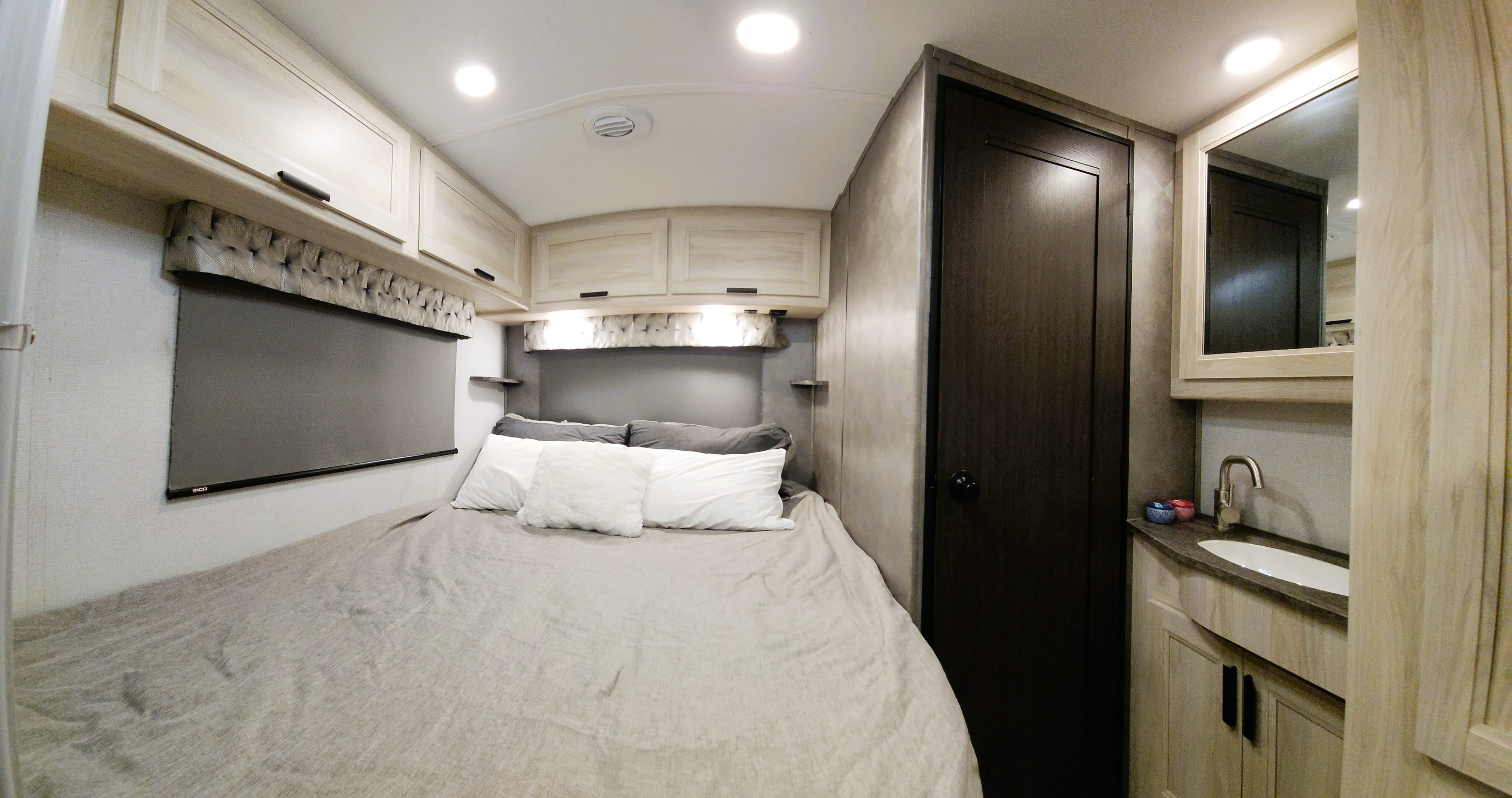 Cozy RV rental bedroom. Features a light-toned interior, full bed, overhead storage, and a compact sink area.. Forest River Sunseeker LE 2022