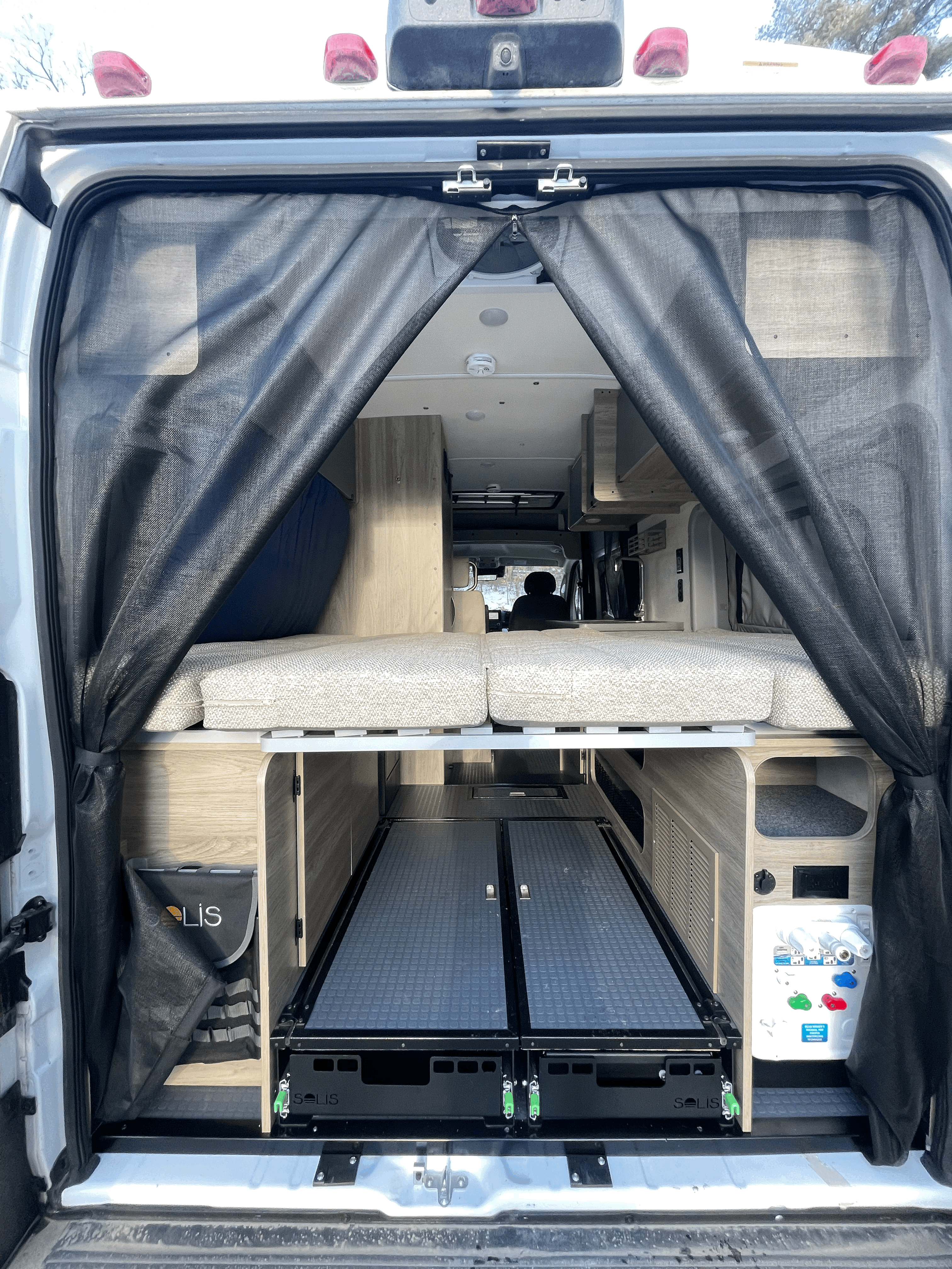 Rear view of an rv rental camper van's interior, showcasing a mesh screen, raised bed, and pull-out storage.. Winnebago Solis 2023