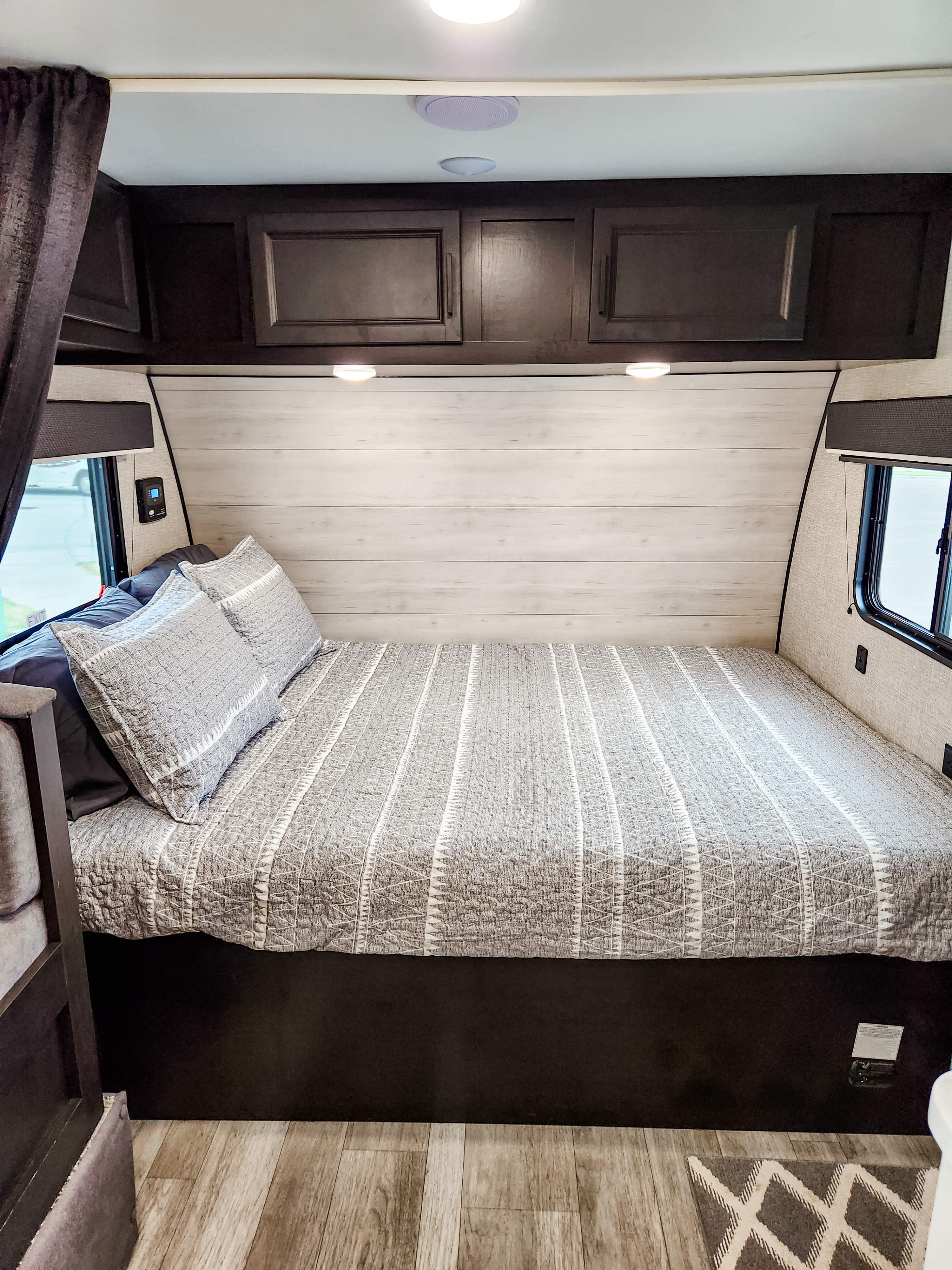 Cozy RV rental bedroom featuring a striped bed, overhead storage, and light wood accent wall. Ideal for travel comfort.. Jayco Jay Flight SLX 2023
