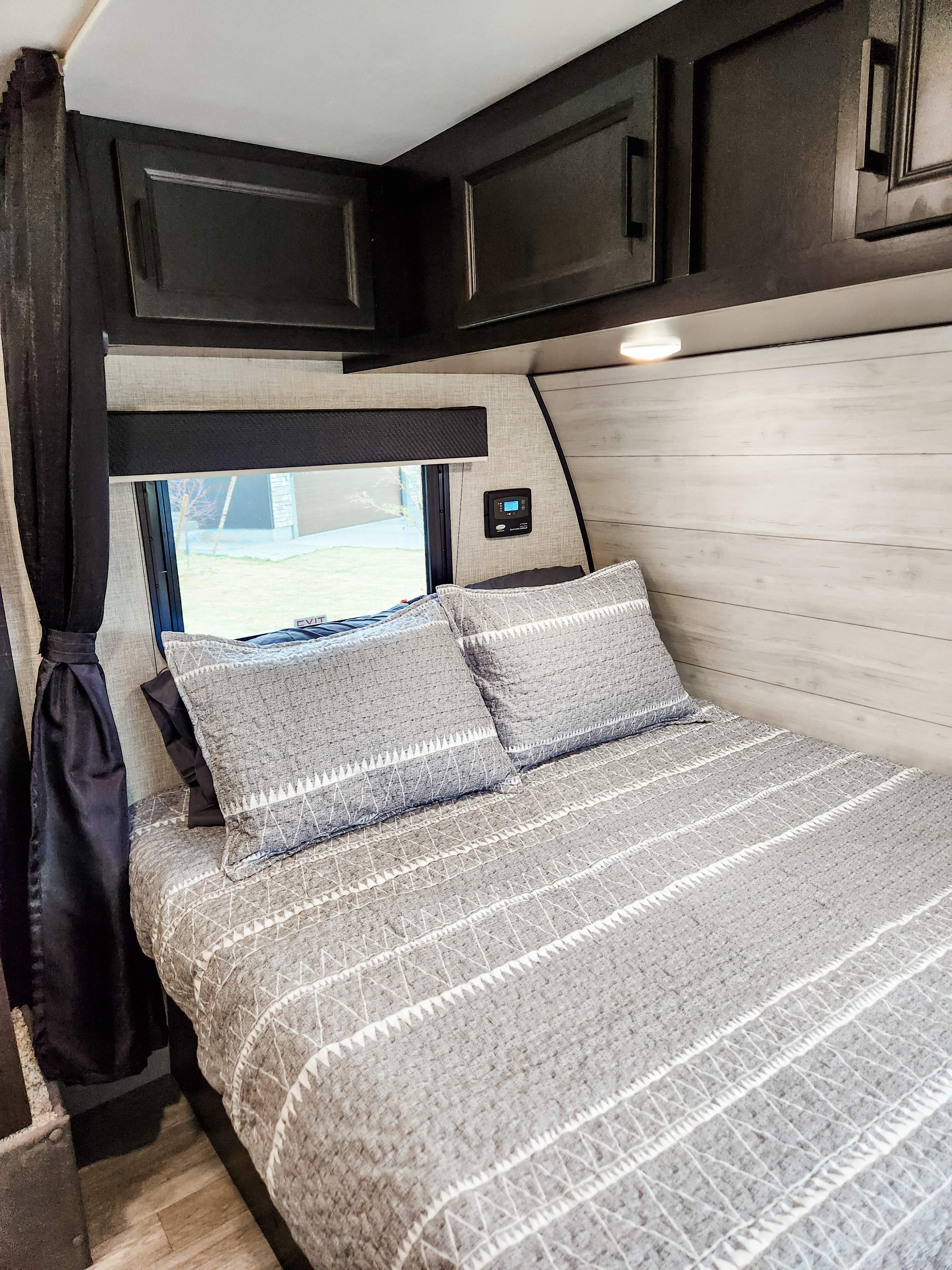 Cozy RV rental bedroom with gray patterned bedding, dark overhead cabinets, and a window, ideal for travel comfort.. Jayco Jay Flight SLX 2023