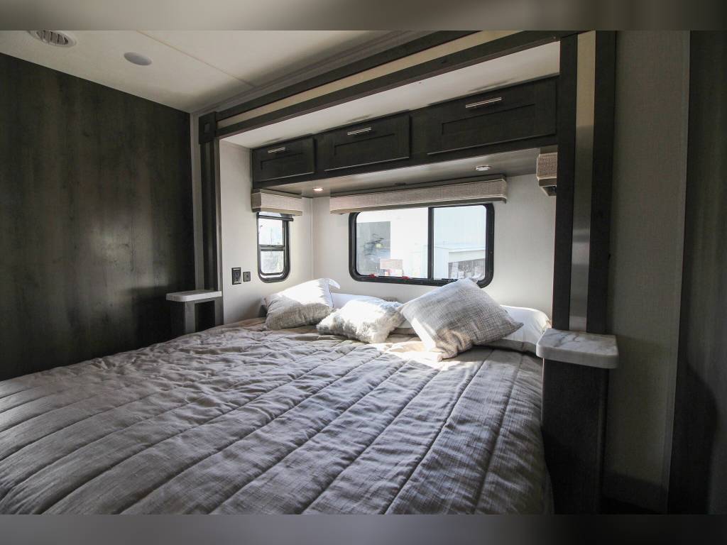Comfortable, modern bedroom in an RV rental, featuring a large bed, windows, and overhead storage.. Forest River Georgetown 2023