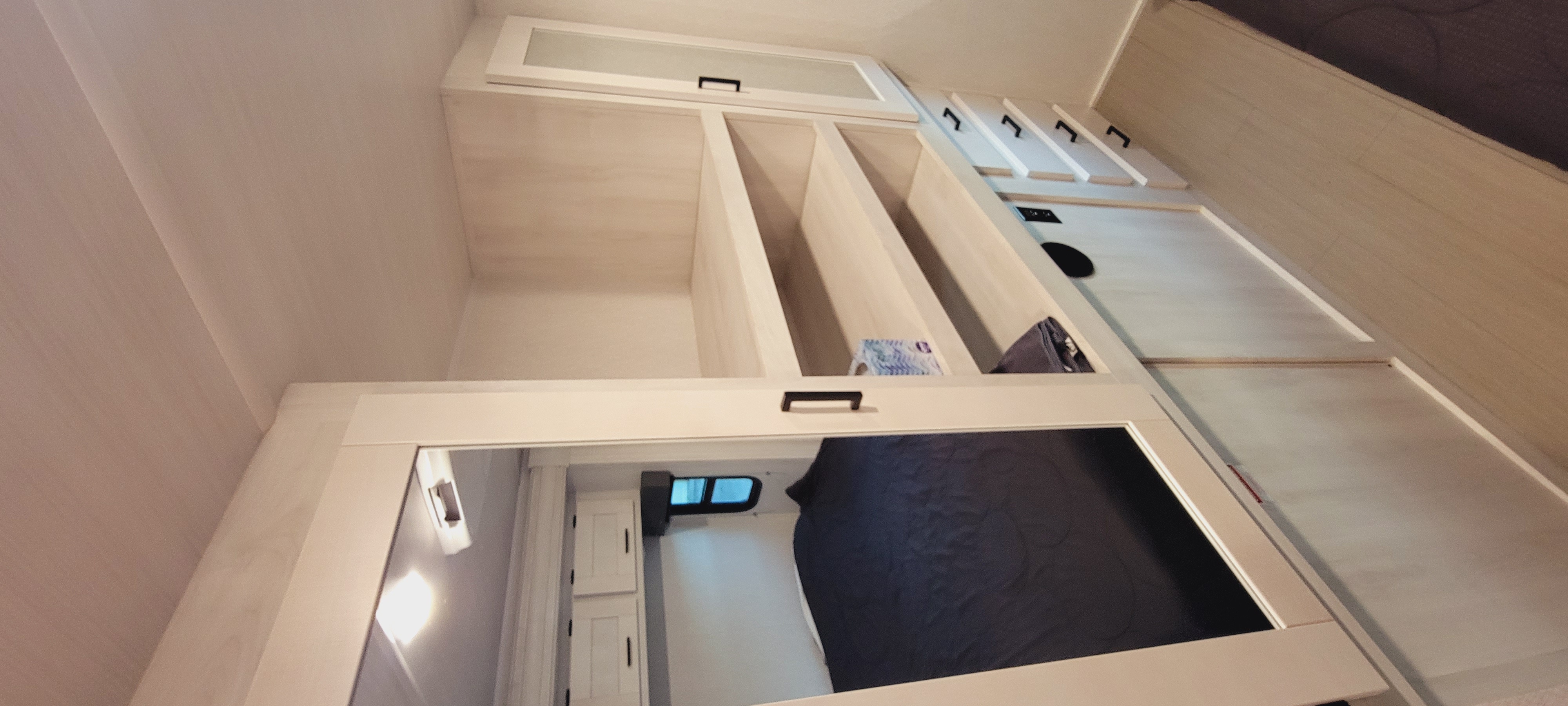 Clean RV rental bedroom with ample storage: open shelves, closed cabinets, and a bed reflected in mirrored closet doors.. East to West 2900DS 2023