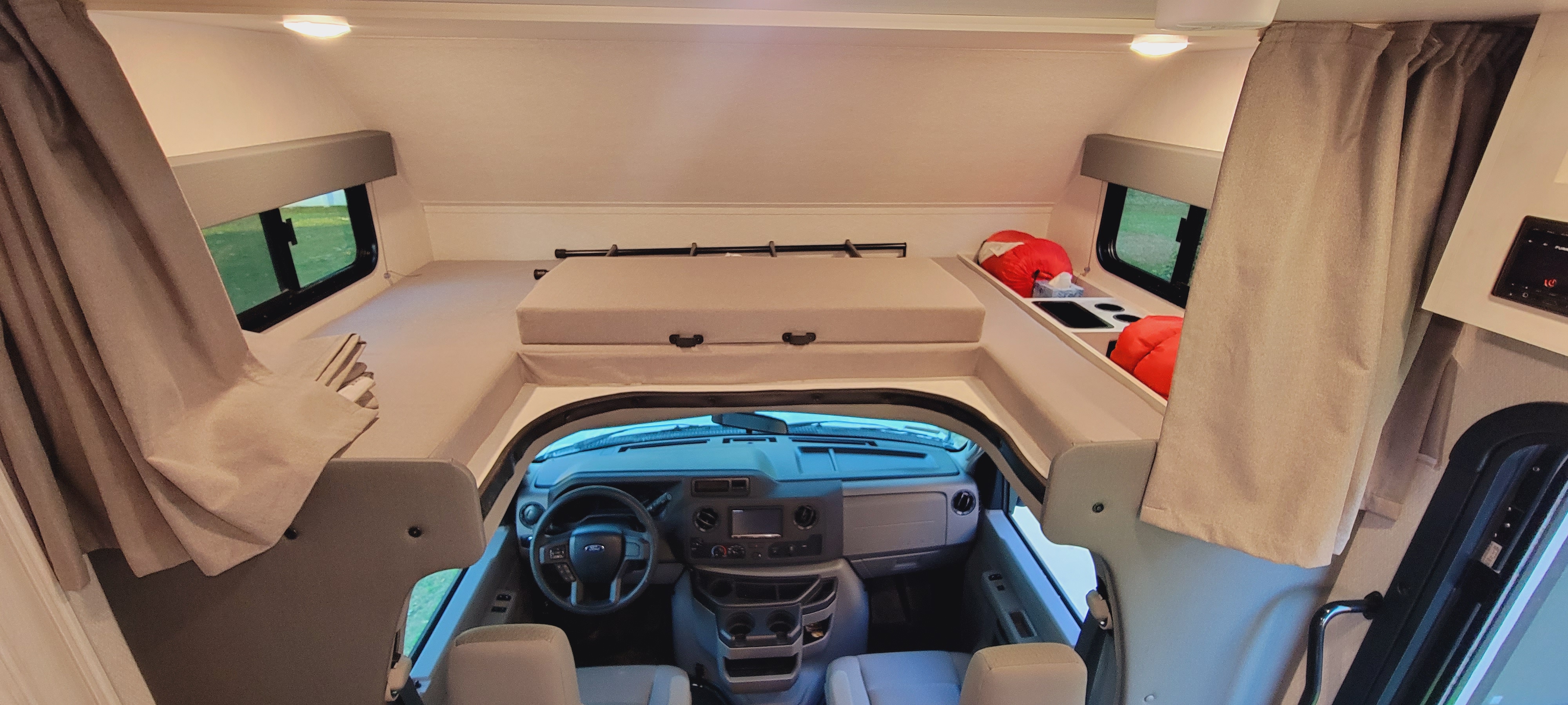 RV rental interior: A wide view of the cab-over bunk bed and the Ford vehicle's cockpit below, with windows and curtains.. East to West 2900DS 2023