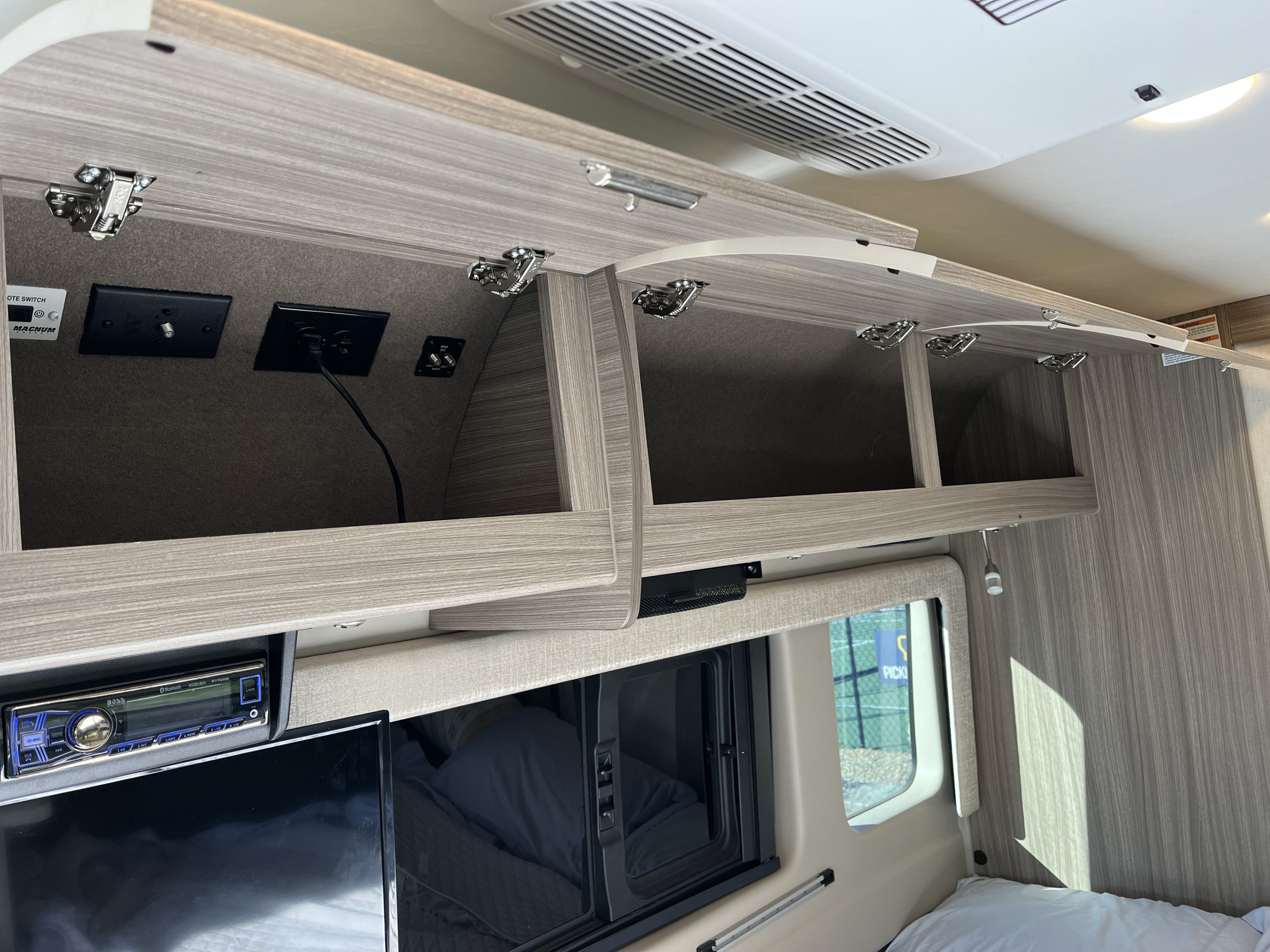 RV rental interior: Open overhead cabinets with power/coax outlets, a stereo, TV, and bed in a modern space.. Jayco Swift 2022
