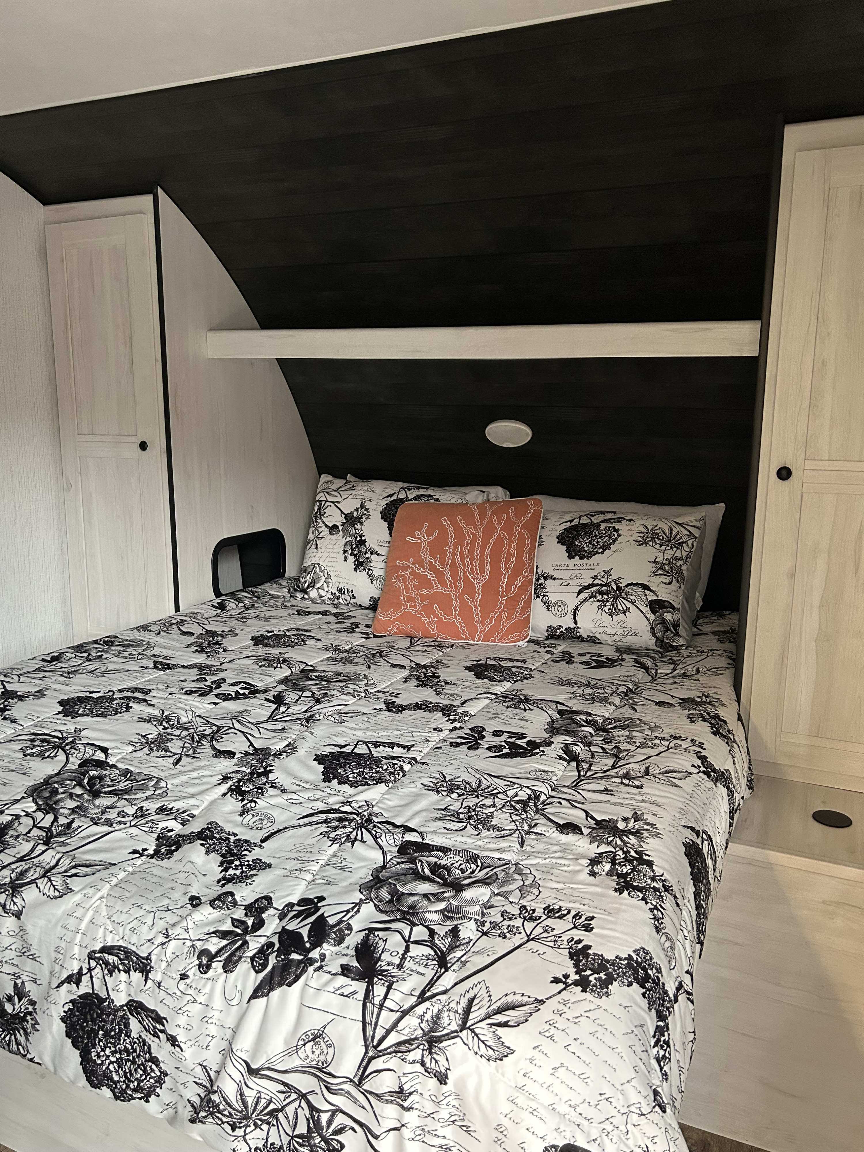 Cozy RV rental bedroom featuring a bed with black and white floral bedding, light wood cabinets, and dark headboard.. Heartland RVs Trail Runner 2022