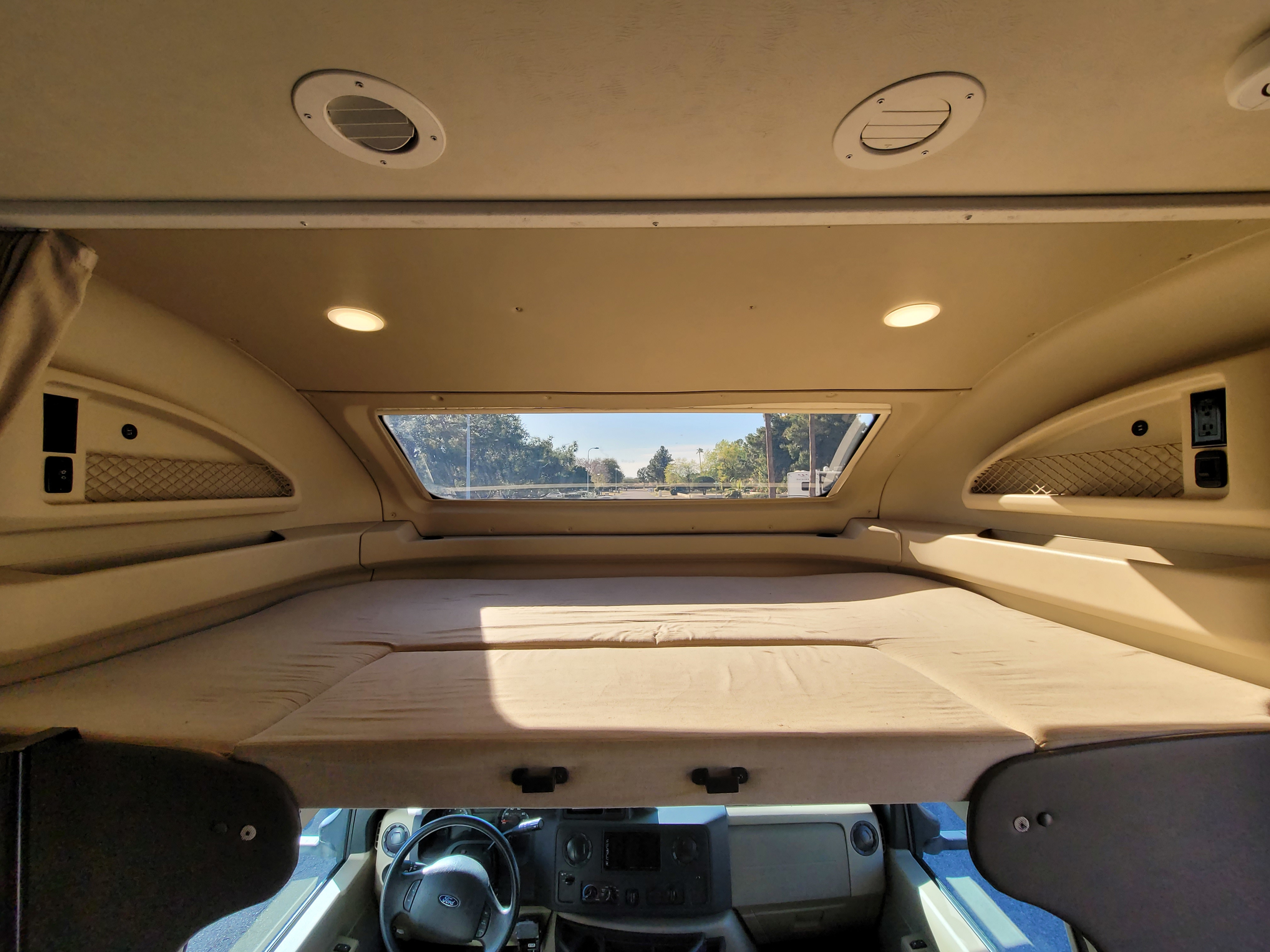 Spacious over-cab bunk in an RV rental, featuring a comfortable sleeping area, overhead window, and convenient power/storage.. Entegra Coach Odyssey 2020