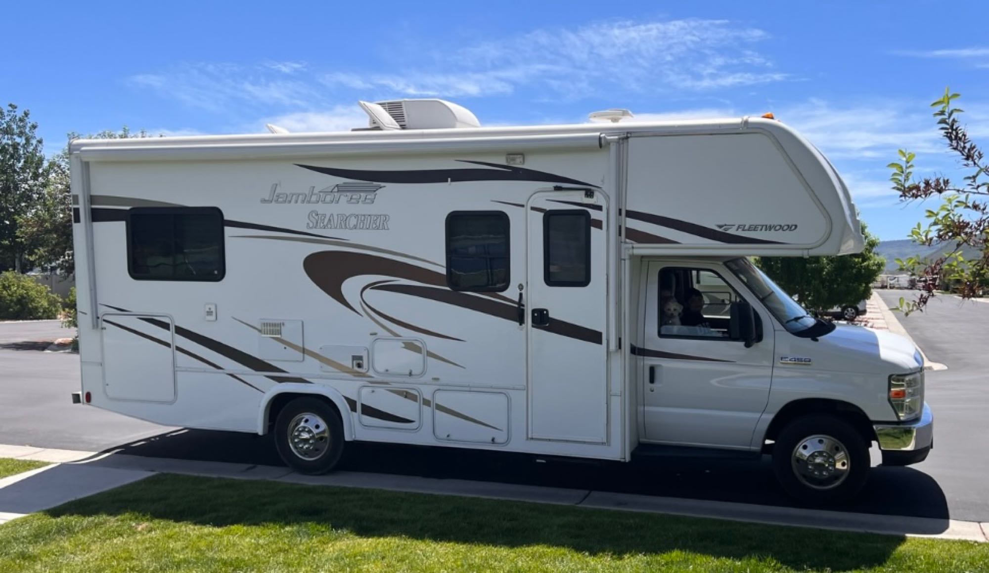 White Fleetwood Jamboree Class C motorhome, ideal for an RV rental adventure. A small dog peeks from the cab window.. Jamboree Searcher 2013