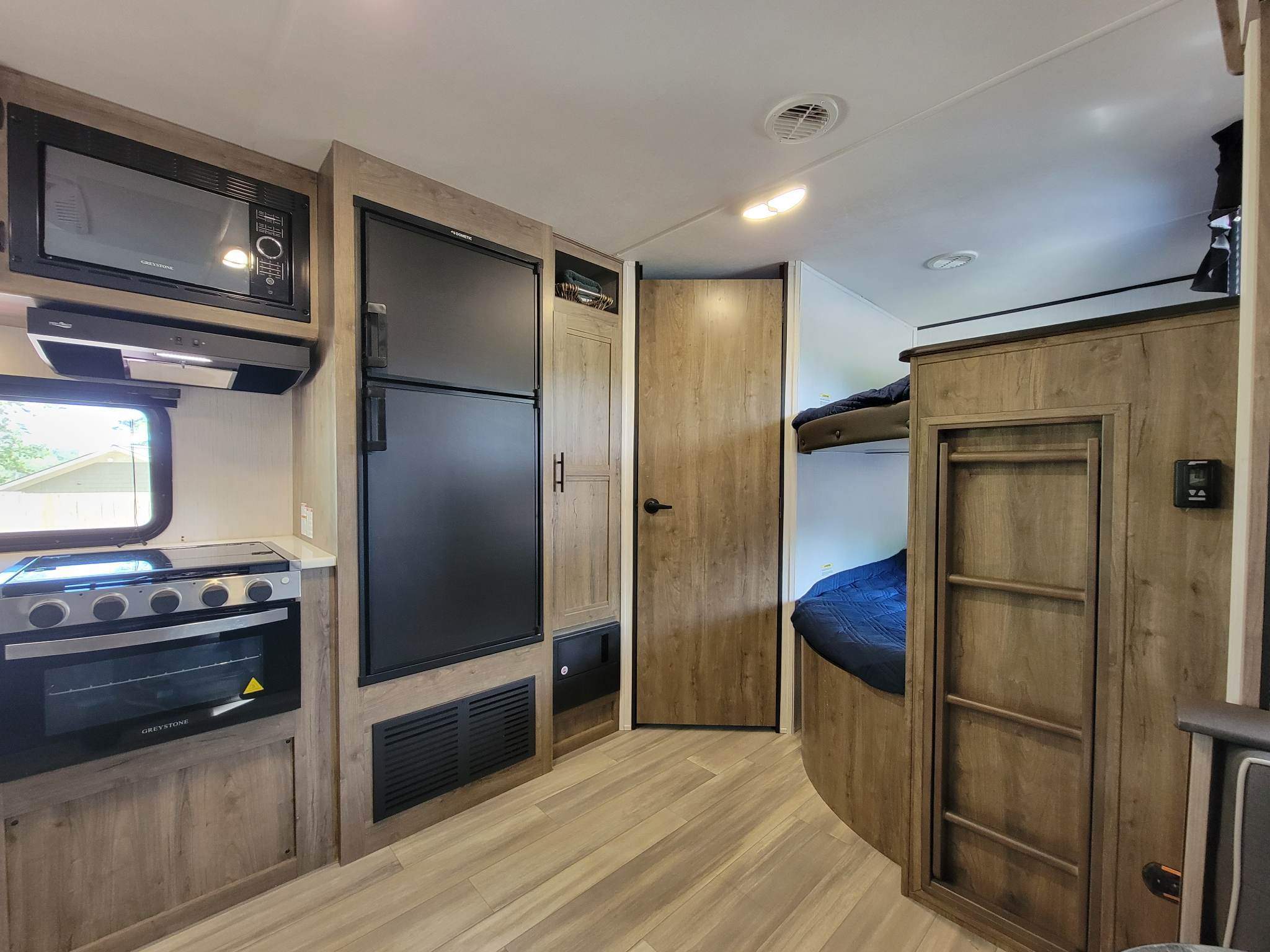 Modern RV rental interior: kitchen with microwave, stove, oven, fridge on left, and integrated bunk beds on right.. Heartland RVs Pioneer 2021