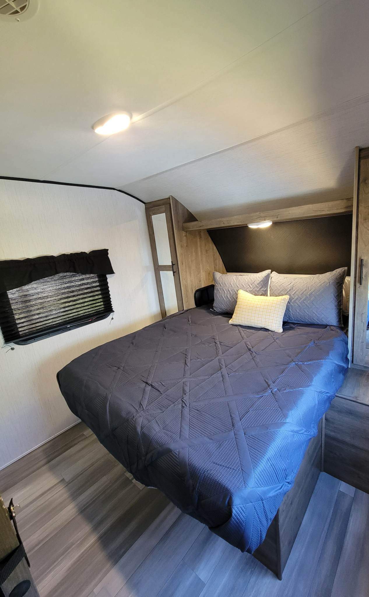 Relax in this modern RV rental bedroom. It features a comfortable bed with grey pillows, integrated storage, and a window.. Heartland RVs Pioneer 2021