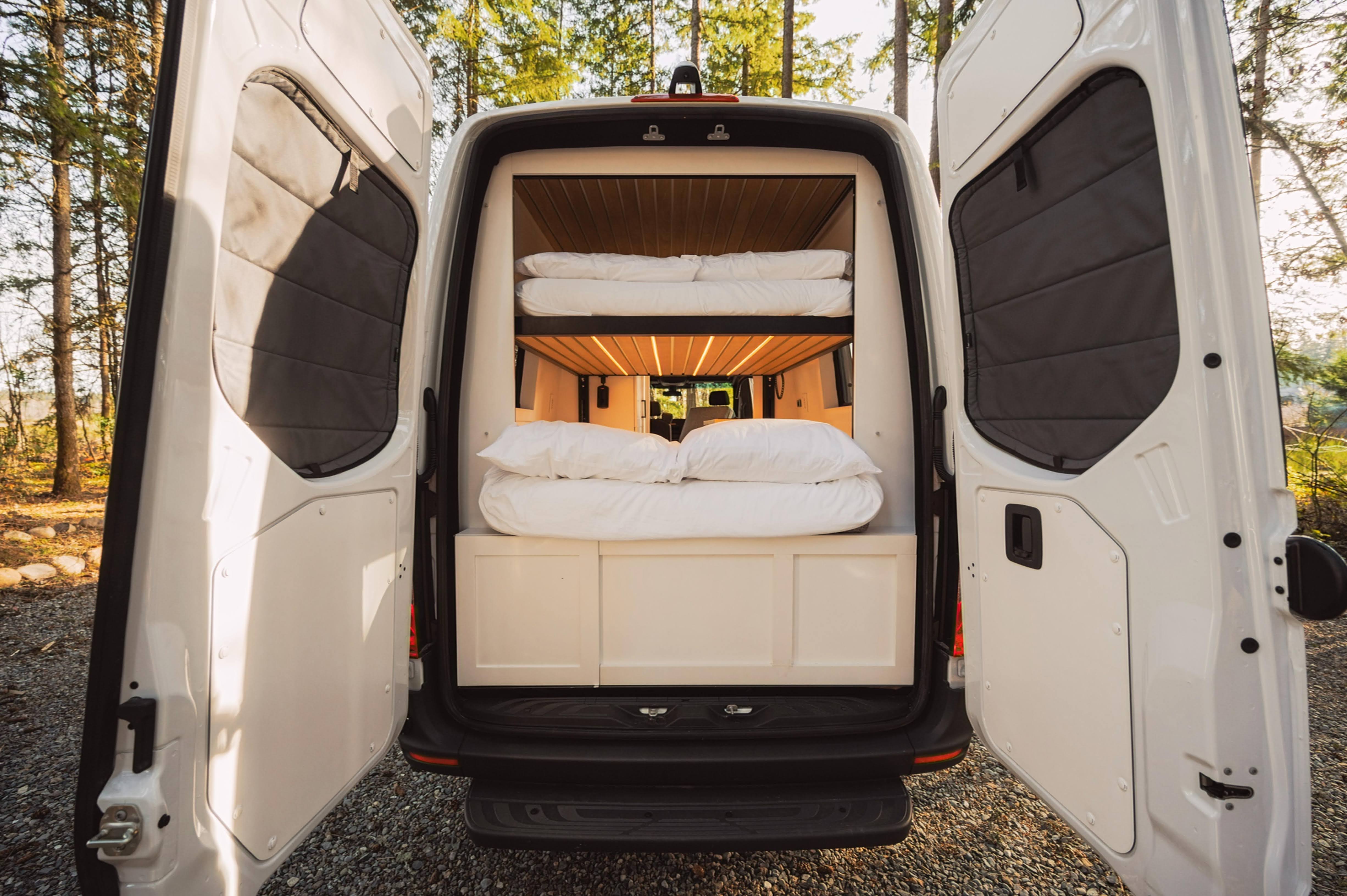 This RV rental's rear doors open to a well-lit interior with comfy bunk beds, ready for travel.. Mercedes-Benz Sprinter 2021