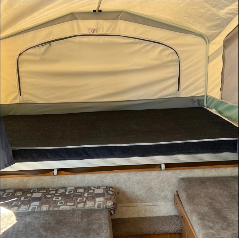 Pop-up RV rental interior: a comfy bed with black mattress & an 'EXIT' sign above.. Forest River Palomino 2010