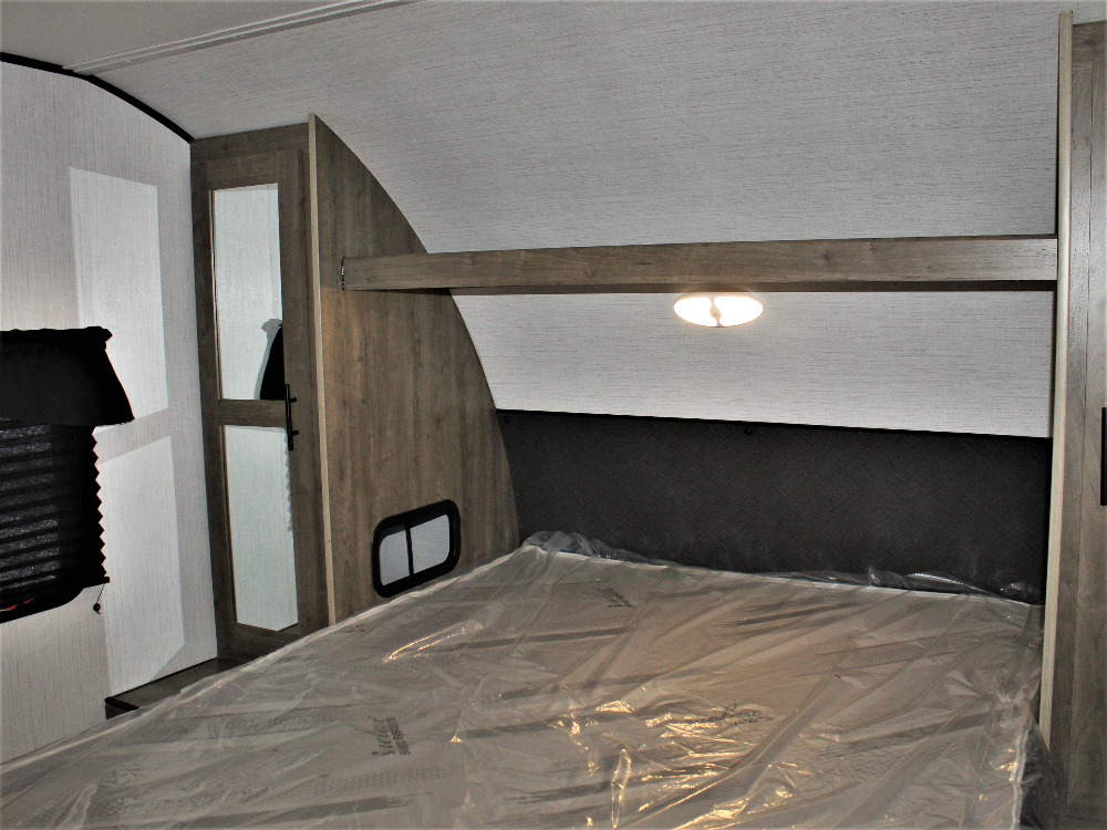 Clean RV rental bedroom with new plastic-wrapped mattress, integrated storage, and overhead light. Ready for comfortable travel.. Heartland RVs Pioneer 2023