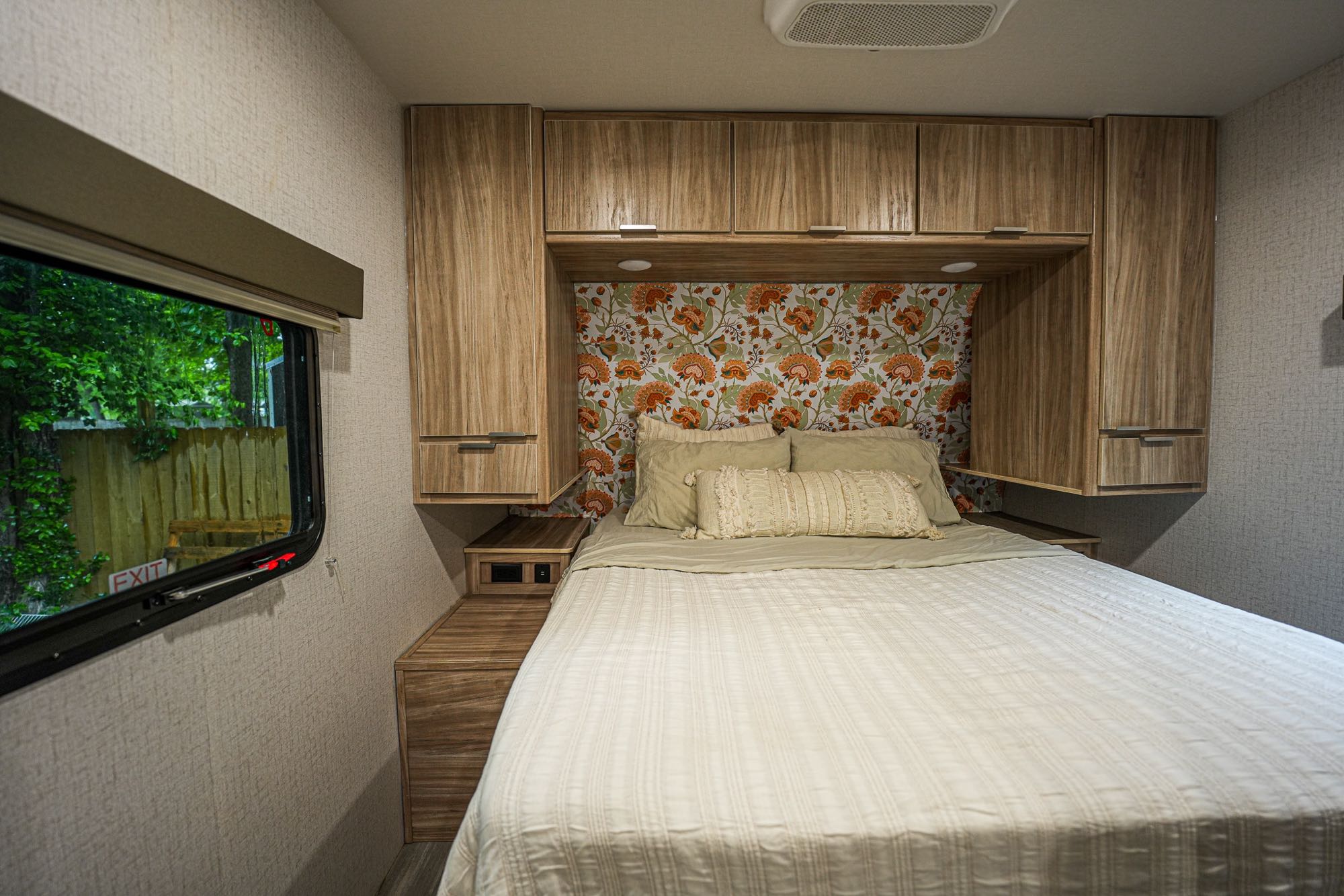 Cozy RV rental bedroom features a queen bed, wood-grain cabinetry, and a vibrant floral accent wall. Enjoy nature views from the window.. Winnebago Minnie 2022