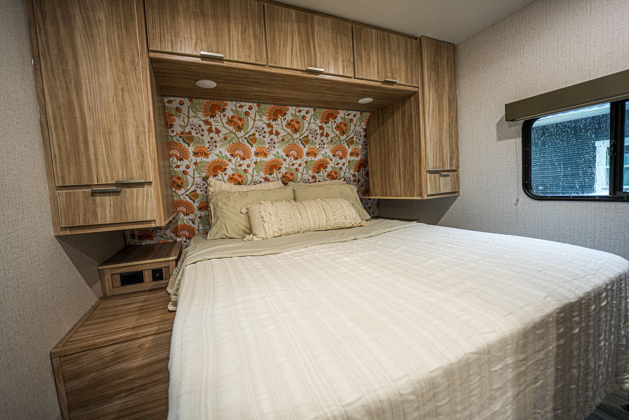Cozy RV rental bedroom featuring a large bed, light-colored comforter, wooden overhead cabinets, and a vibrant floral headboard.. Winnebago Minnie 2022