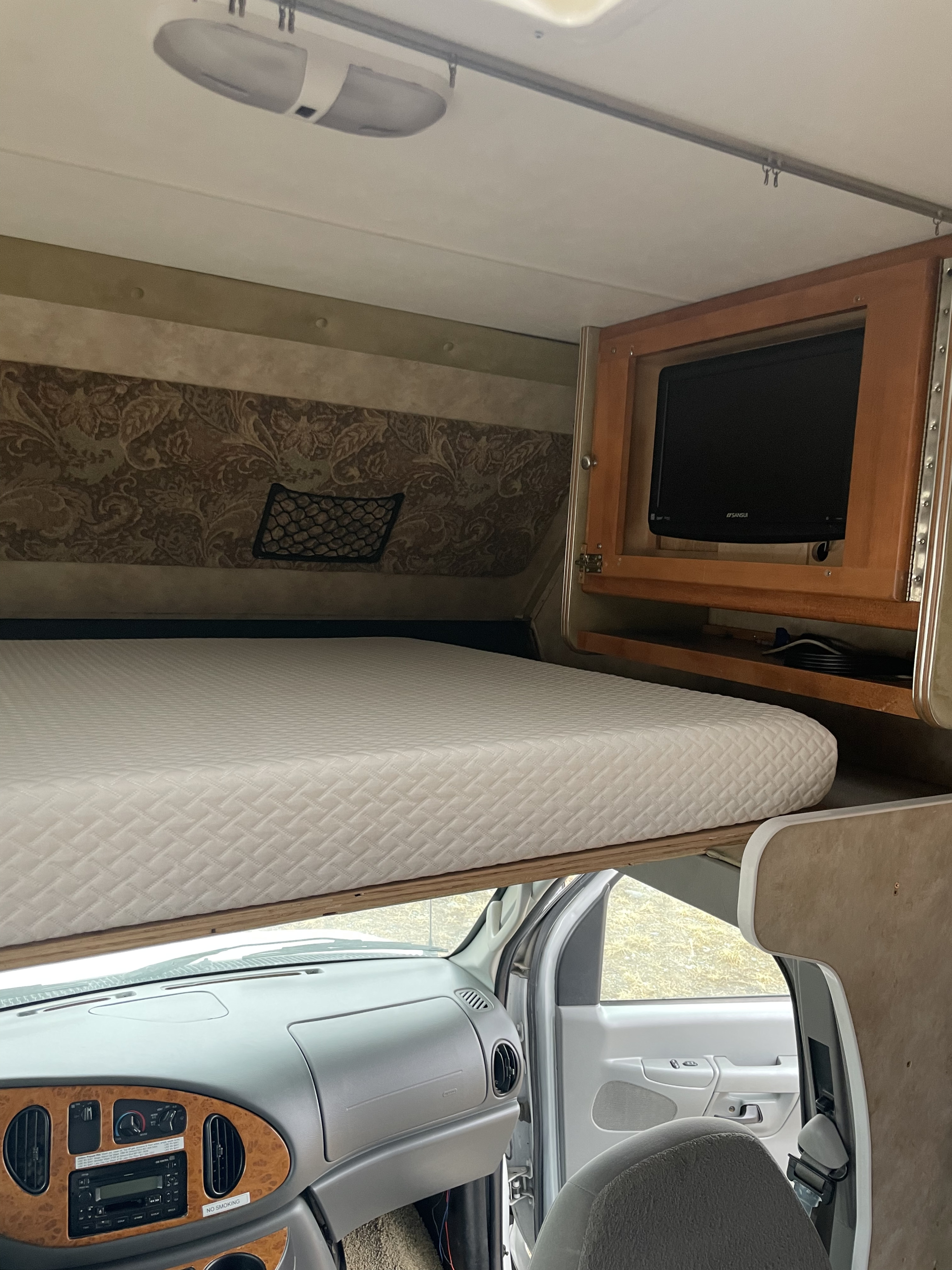 Inside an RV rental: a comfortable cab-over bunk bed with quilted mattress, built-in TV, and driver's cabin view.. Gulf Stream Yellowstone 2008