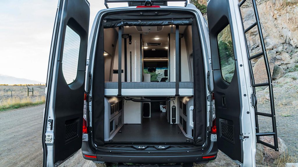 RV rental: Back of a versatile camper van with open doors, revealing an elevated bed and spacious gear area.. Winnebago Revel 2022