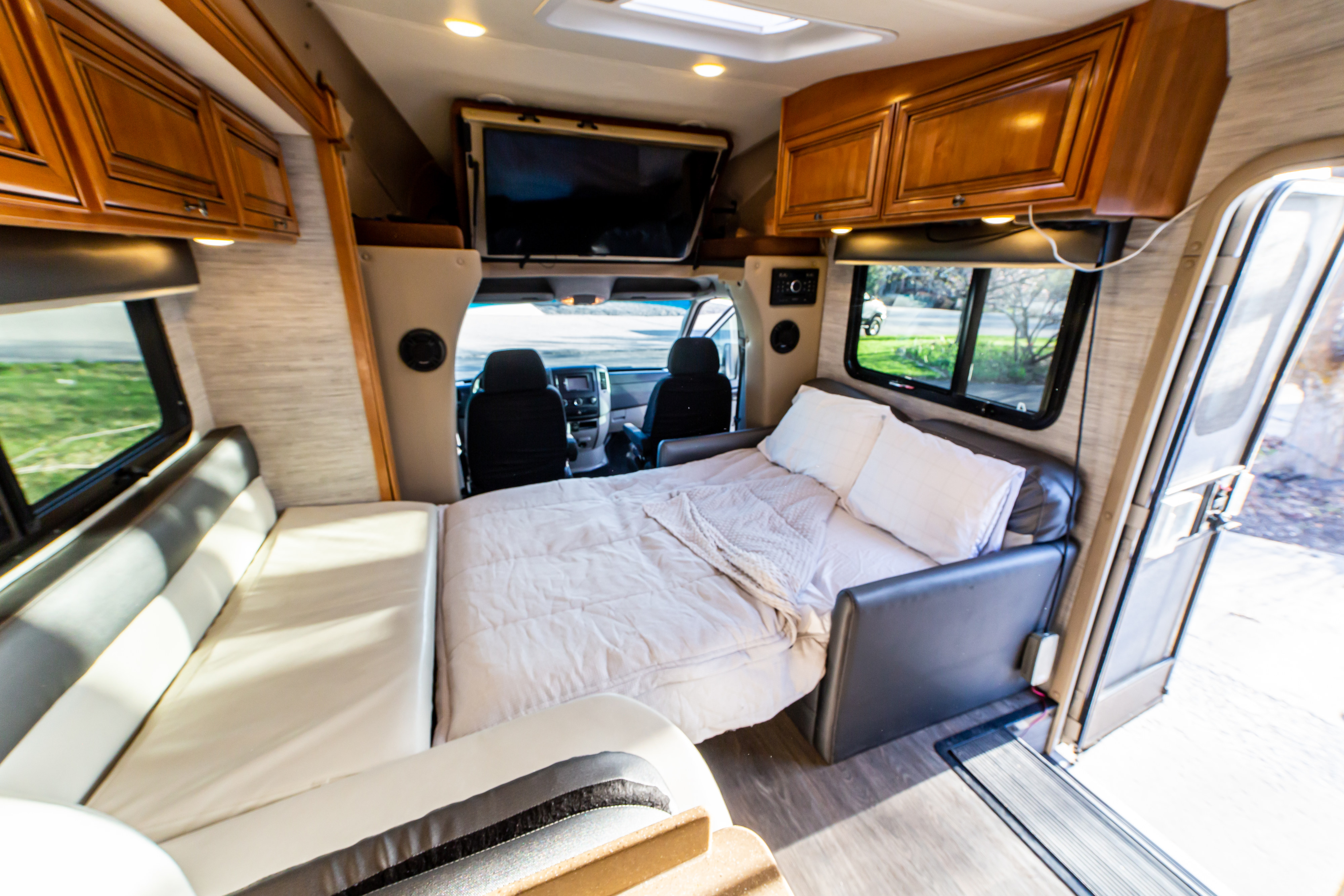 Comfortable RV rental interior: a bed setup on the right, lounge seating on the left, and a view into the driver's cab.. Thor Citation Sprinter 2016