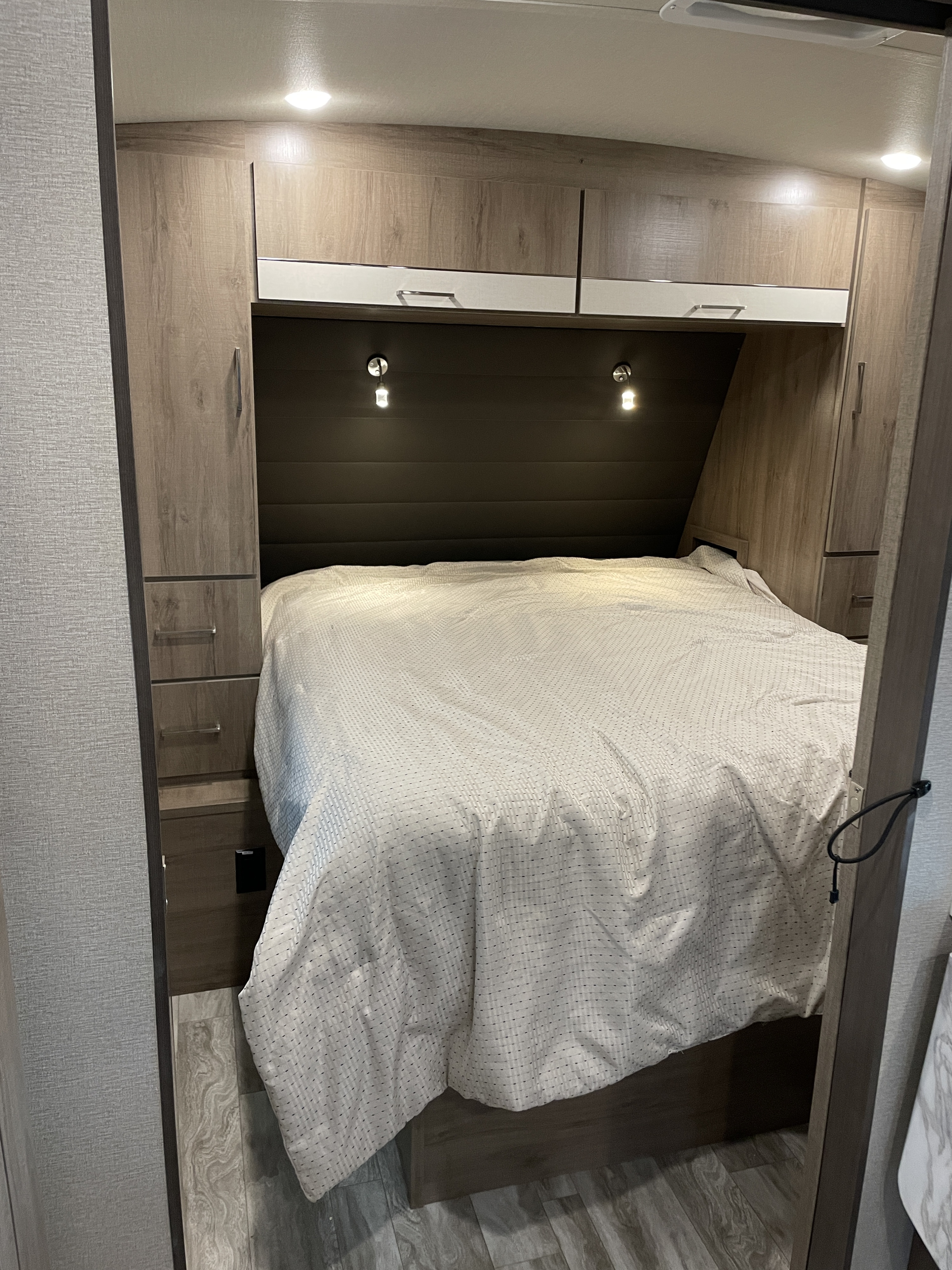 Spacious RV rental bedroom featuring a queen bed, reading lights, and built-in wood-look cabinetry.. Grand Design Imagine 2022