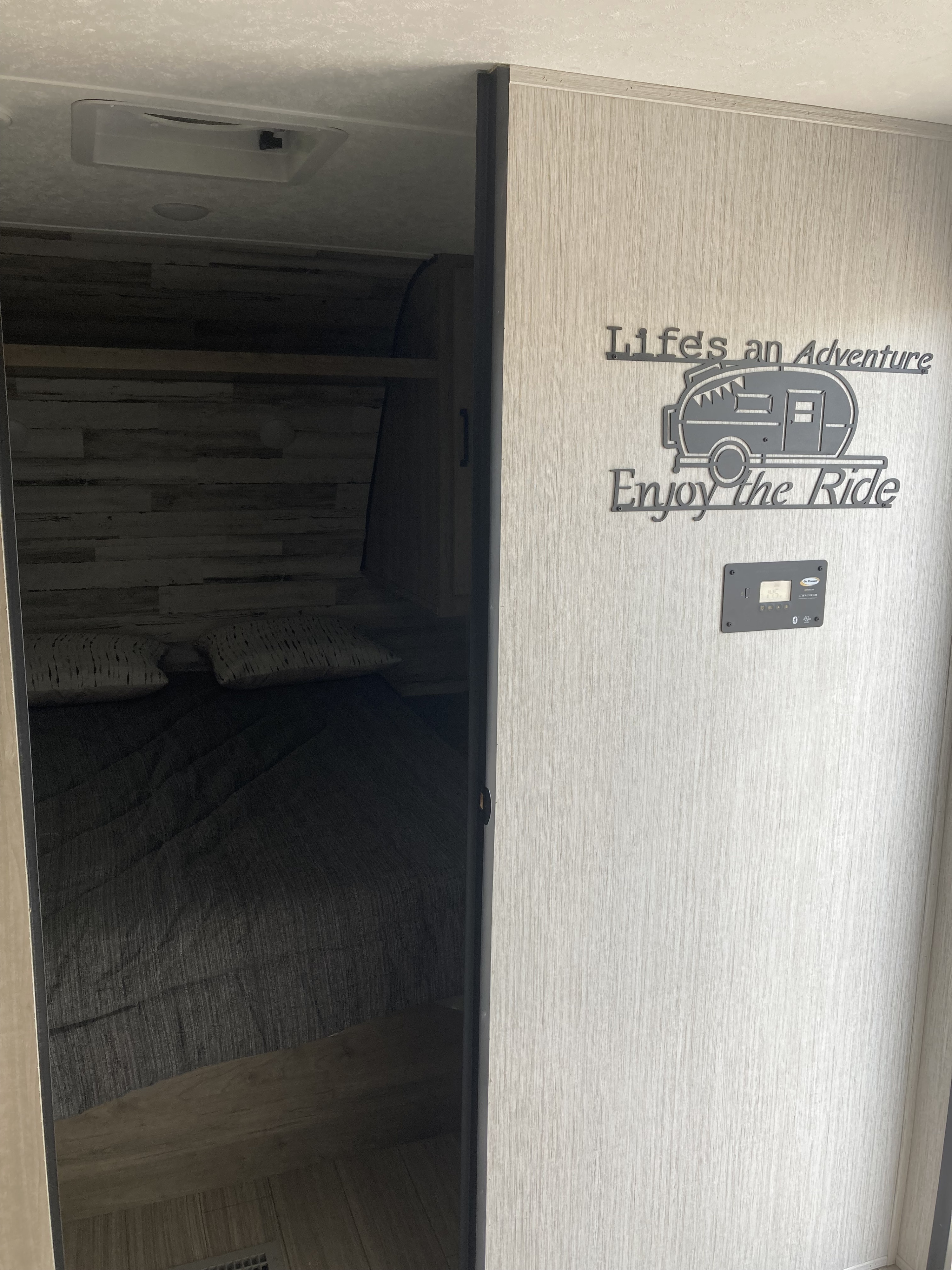 RV rental interior with bedroom visible through a sliding door, featuring a "Life's an Adventure" sign and control panel.. Palomino Puma XLE 2022