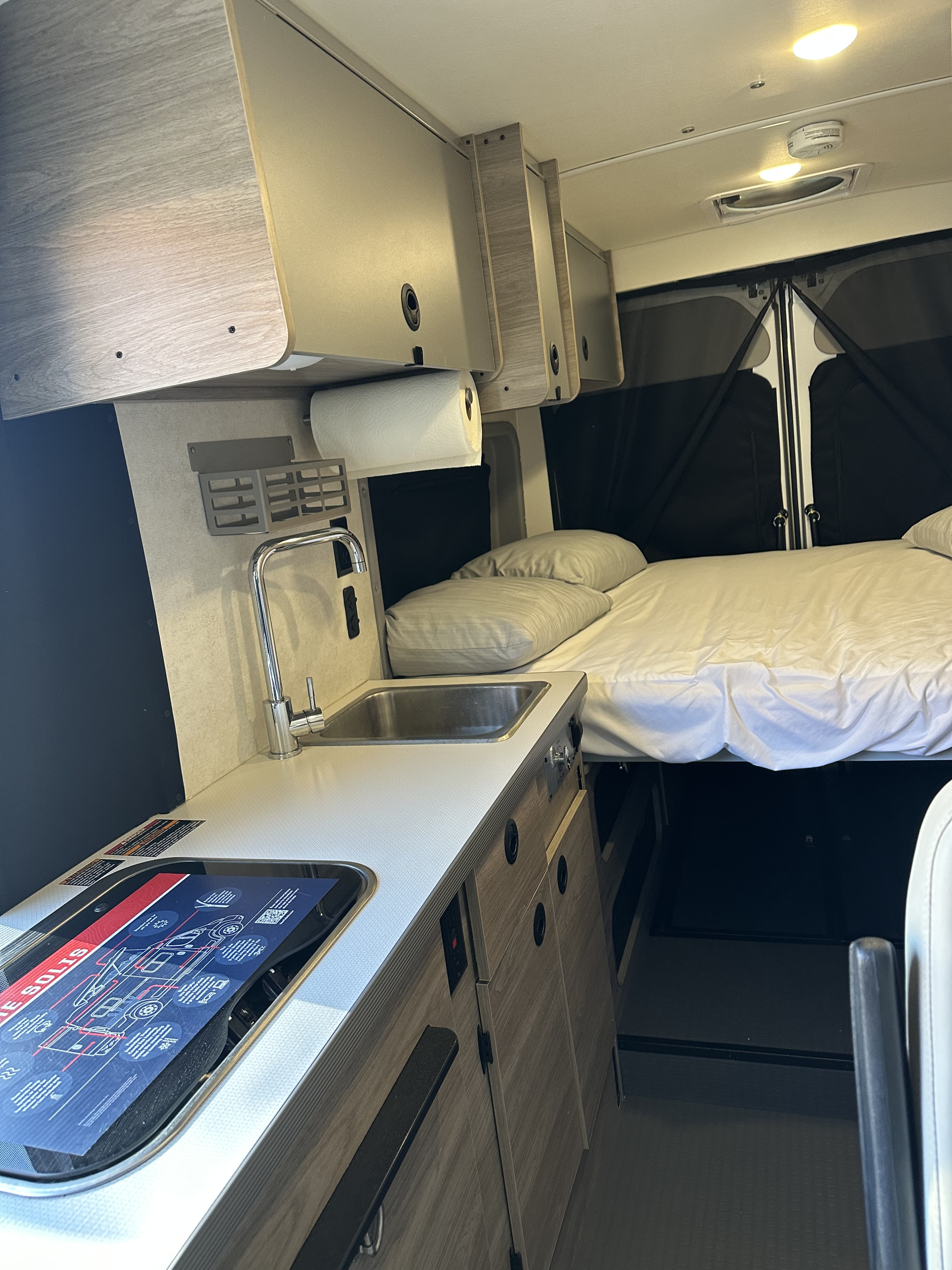Bright RV rental interior featuring a practical kitchen with sink/stove and a comfy bed. Essential amenities for travel.. 2023 Winnebage Ram Pro master 3500 2023