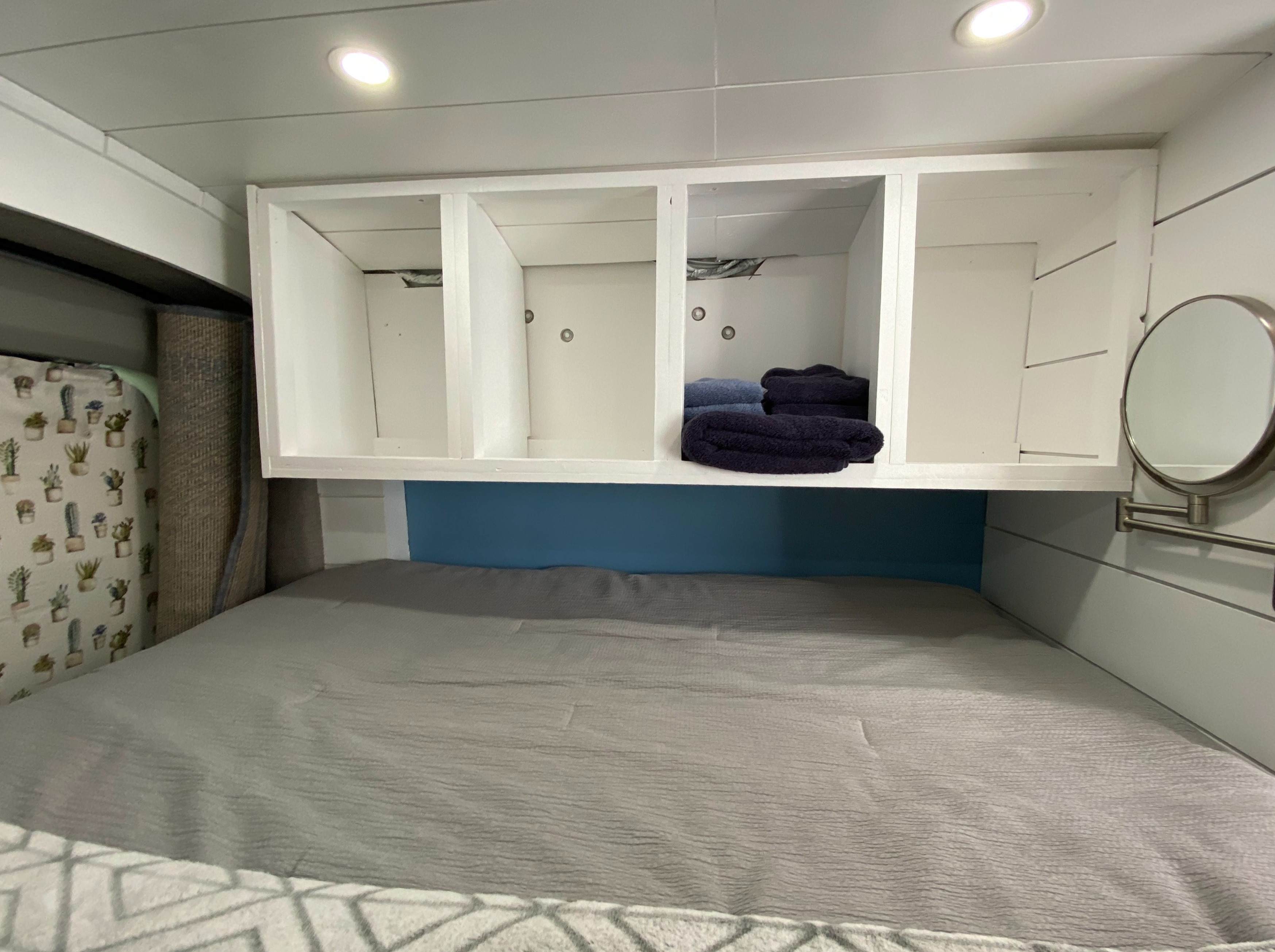Inside an RV rental: a cozy bed, white storage cubbies with folded towels, and a blue accent wall. Compact and functional space.. Ford Transit Custom 2015