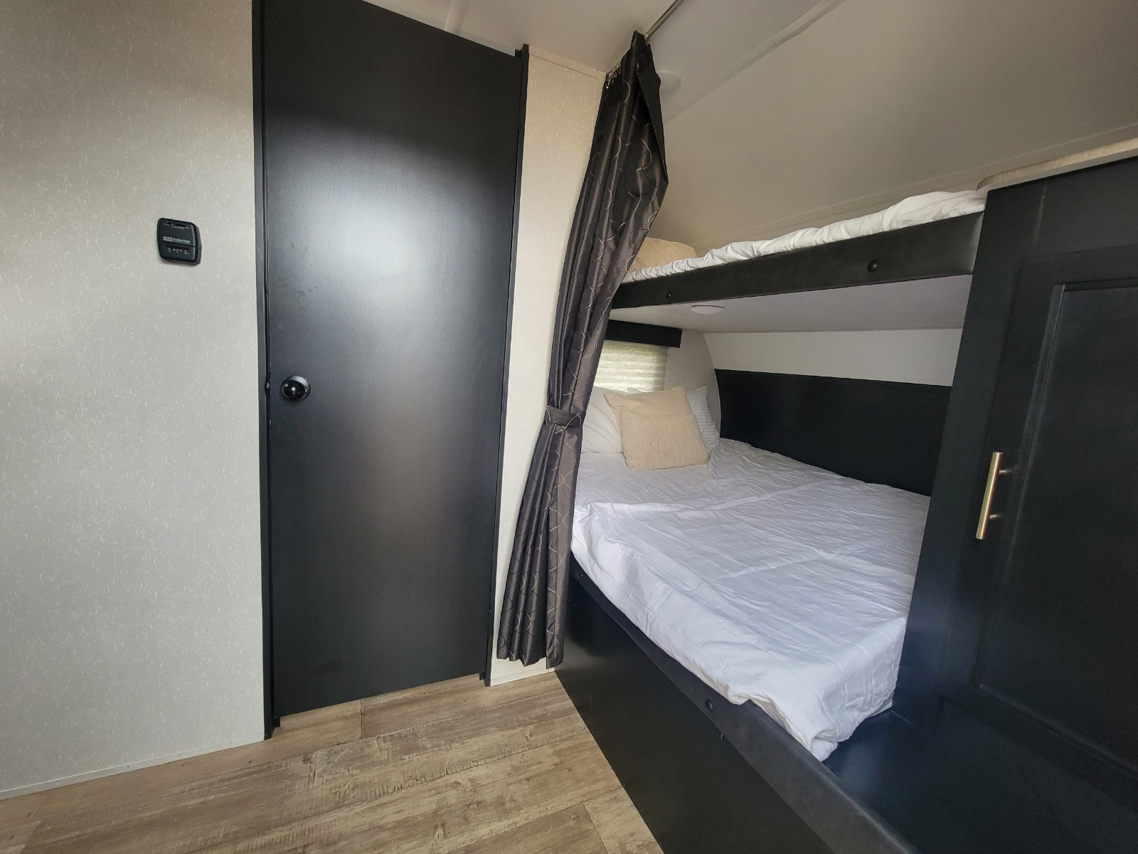 Inside an RV rental, showing a sleeping area with stacked bunk beds, white bedding, a privacy curtain, and a modern dark door.. Forest River Cherokee Grey Wolf 2021