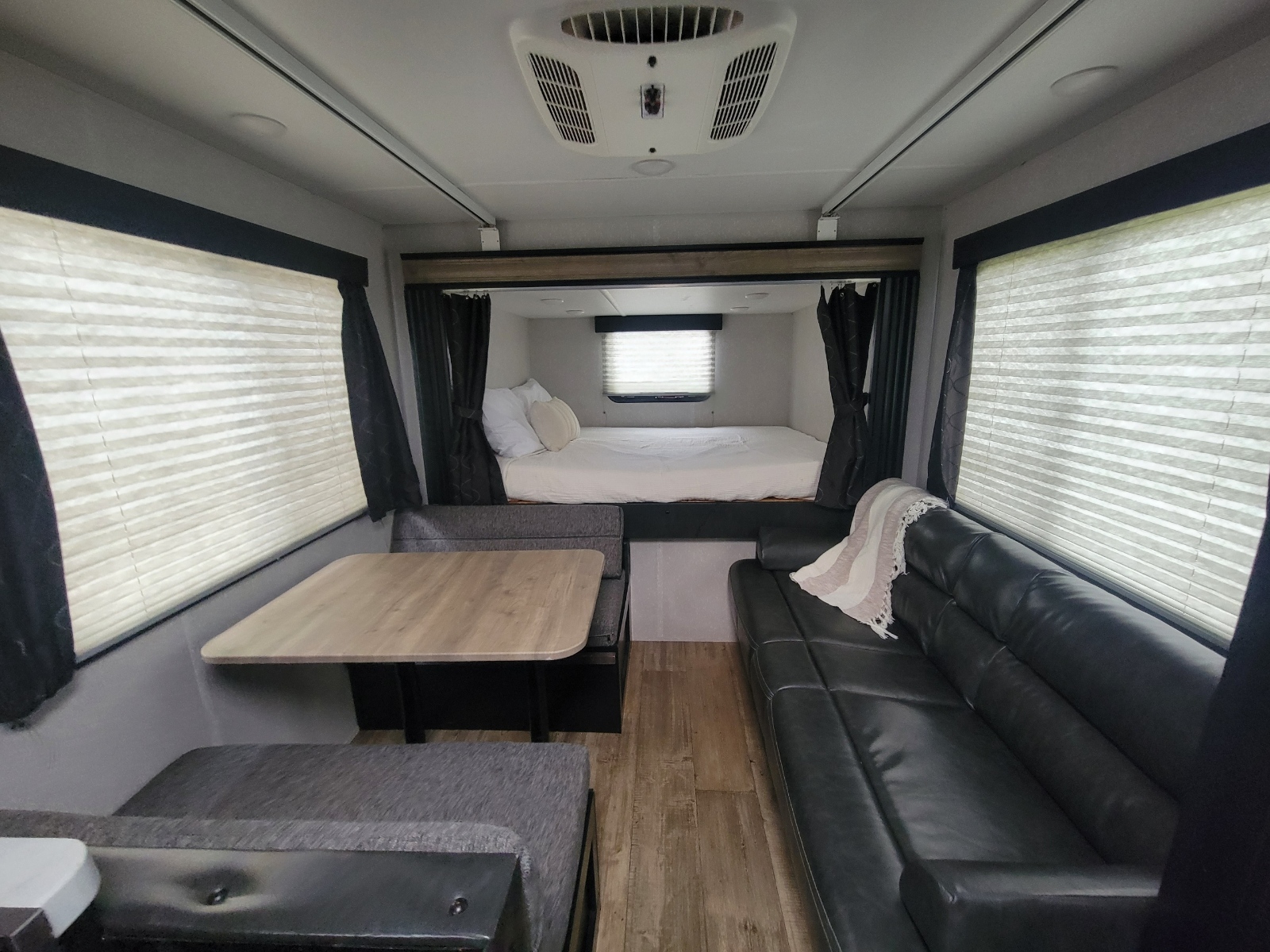 Spacious RV rental interior with a cozy bed, dining area, and comfortable black sofa, perfect for travel.. Forest River Cherokee Grey Wolf 2021