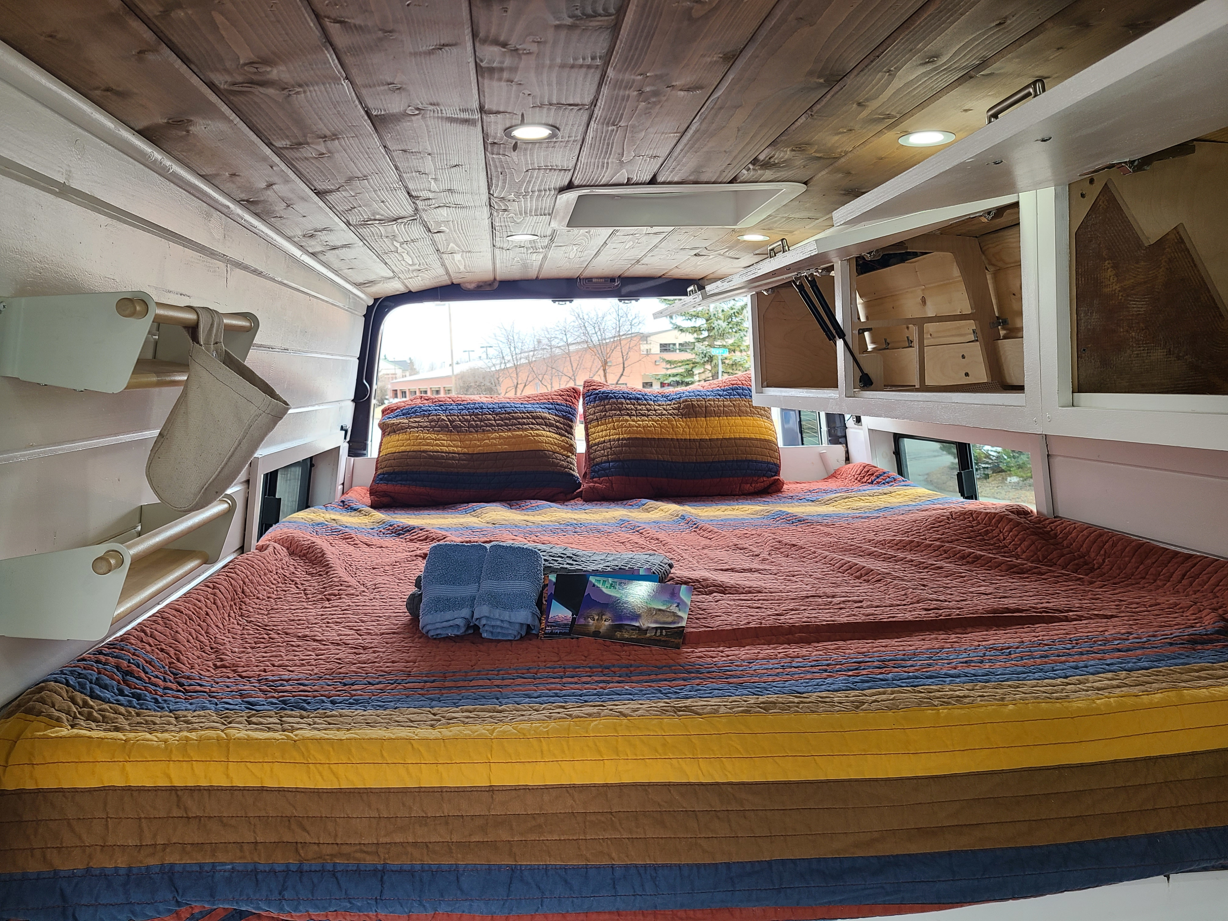 Cozy RV rental interior with a comfortable bed, wooden ceiling, and smart storage. Perfect for your next adventure.. Other Sprinter 2021