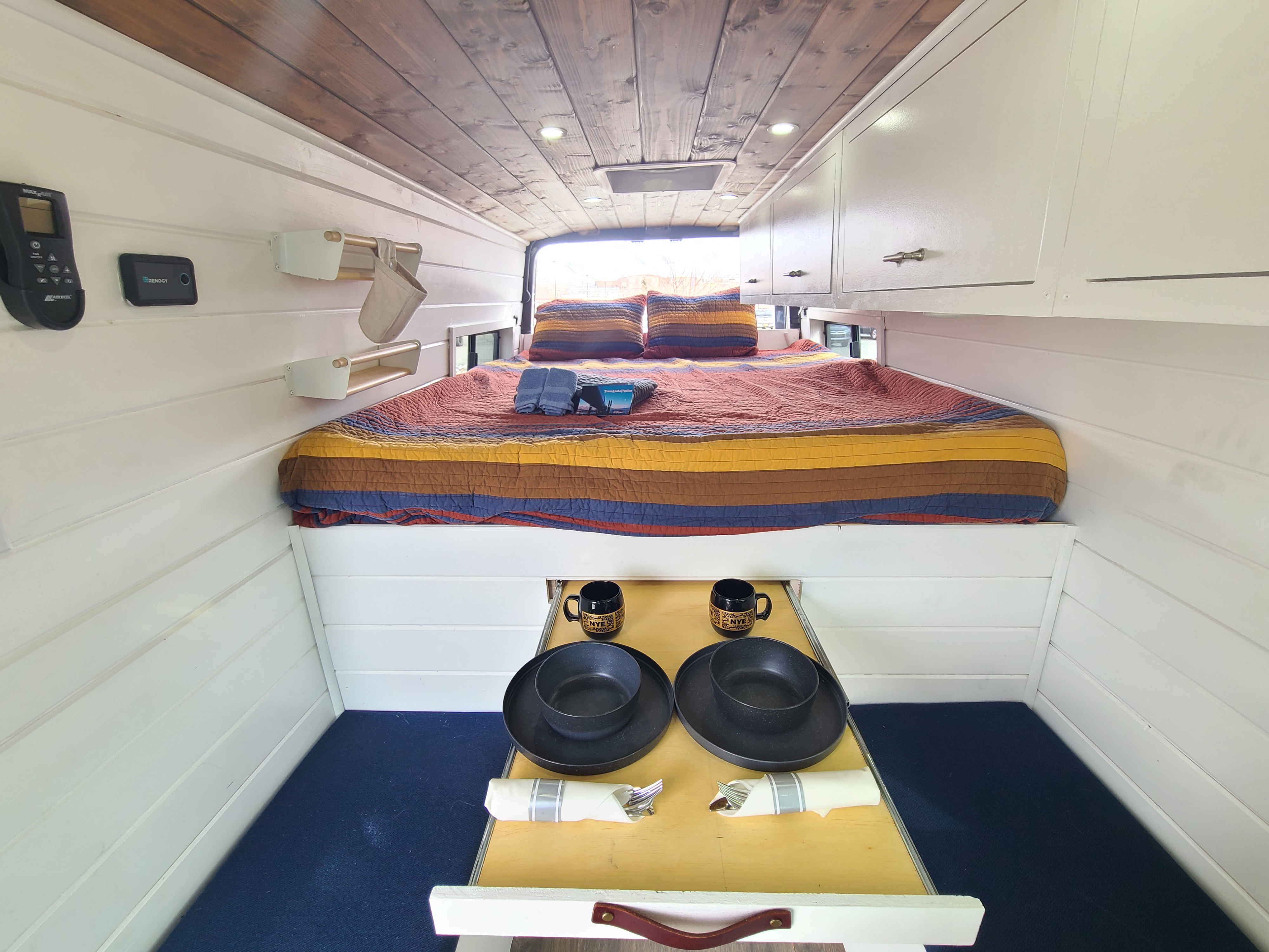 Cozy RV rental interior: elevated bed with colorful quilt, white shiplap walls, wood ceiling, & pull-out dining table.. Other Sprinter 2021