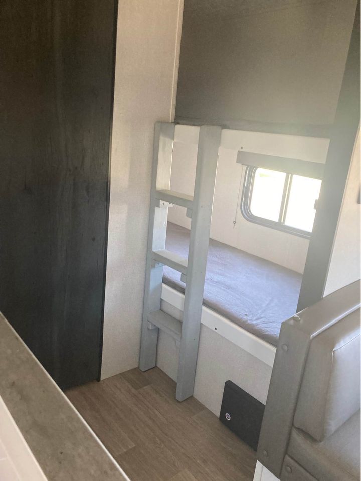RV rental interior: bunk beds with ladder, window, and light wood flooring. A compact sleeping area.. Keystone RV Hideout 2022