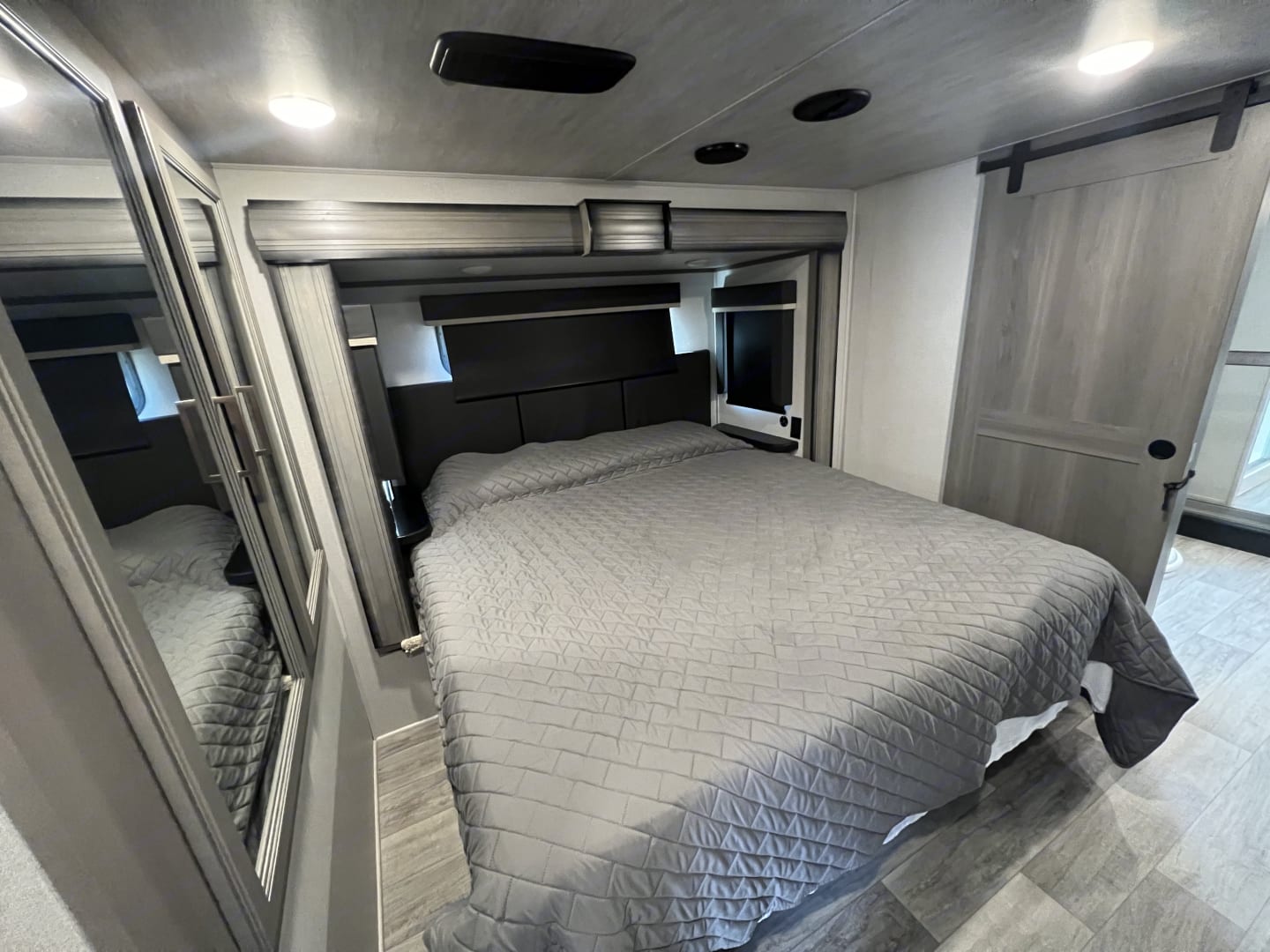 Modern RV rental bedroom features a comfy bed, mirrored closet, and sliding barn door for travel comfort.. Keystone Montana 2021