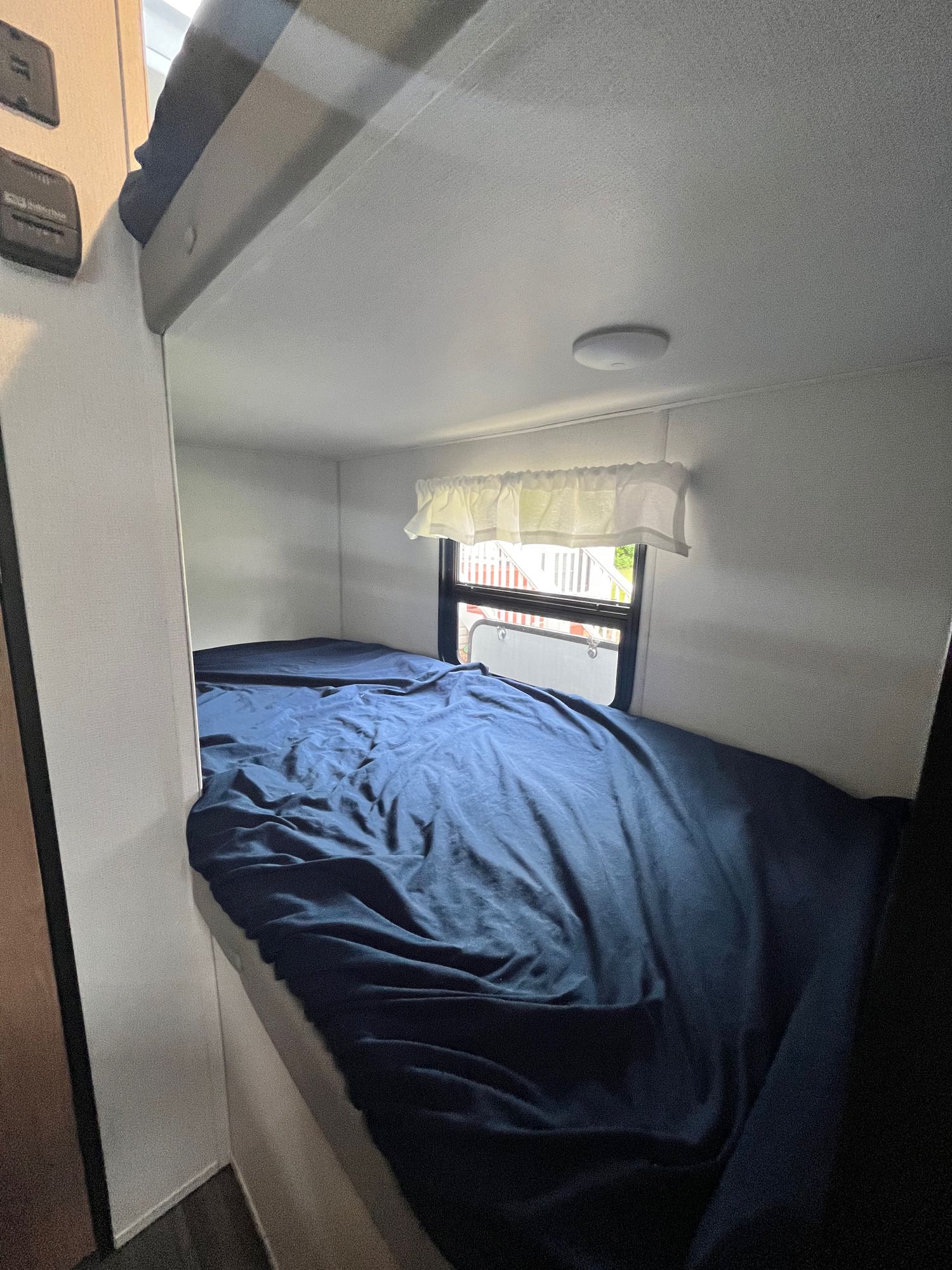 Cozy RV rental bunk bed, featuring dark blue bedding and a window with sheer valance, for comfortable travel.. Avenger LT 2022