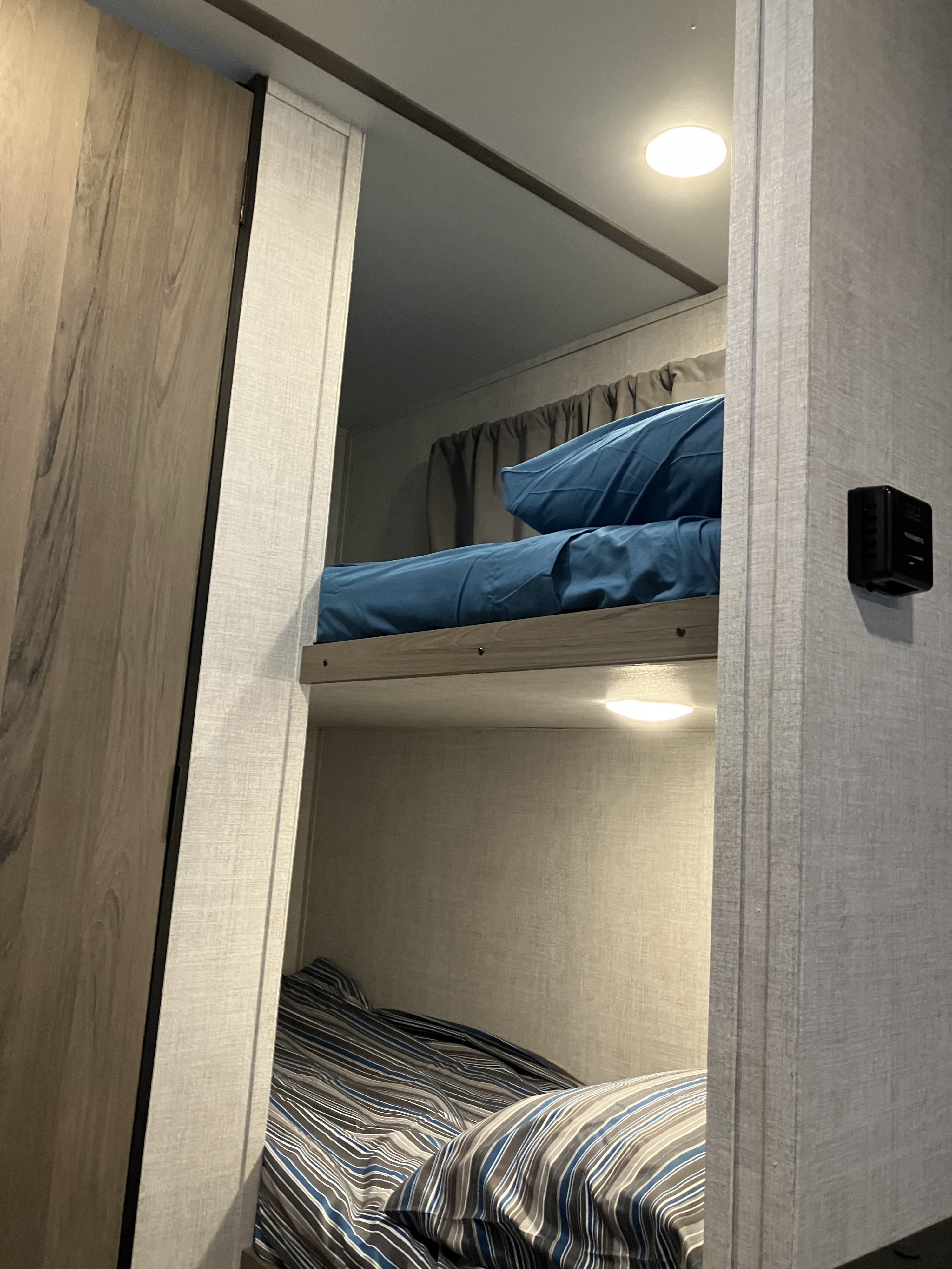 Inside an RV rental: cozy bunk beds, one with blue and one with striped bedding, and interior lighting.. Gulf Stream Ameri-Lite Super Lite 2022