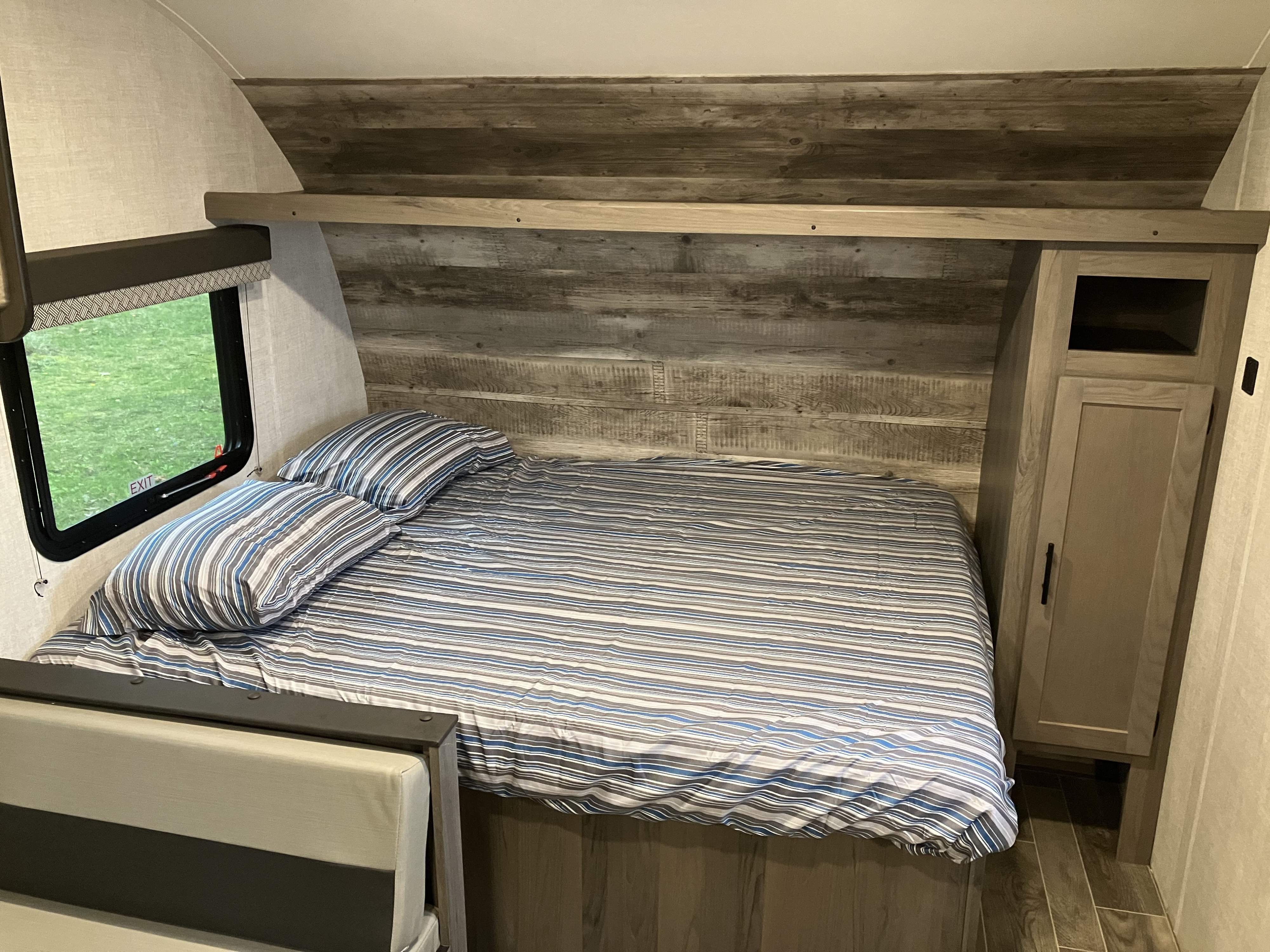 Cozy **RV rental** bedroom with striped bedding, wood accents, and a window overlooking green scenery.. Gulf Stream Ameri-Lite Super Lite 2022