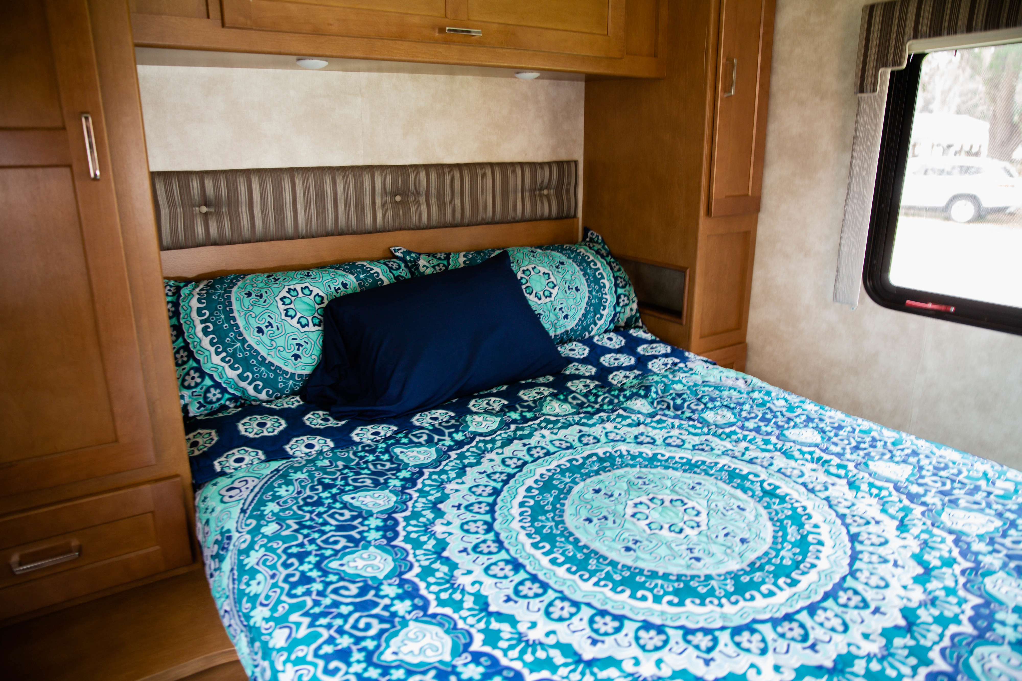 Comfortable RV rental bedroom featuring blue mandala bedding, a striped headboard, and wooden storage cabinets.. Winnebago Spirit 2019