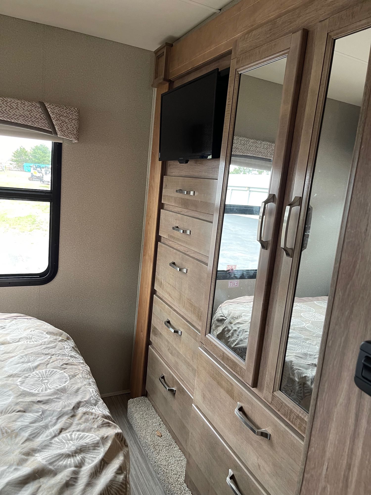 Inside an RV rental: a cozy bedroom with a bed, window, and a wood cabinet featuring a TV, drawers, and a mirrored wardrobe.. Jayco Greyhawk Prestige 2019