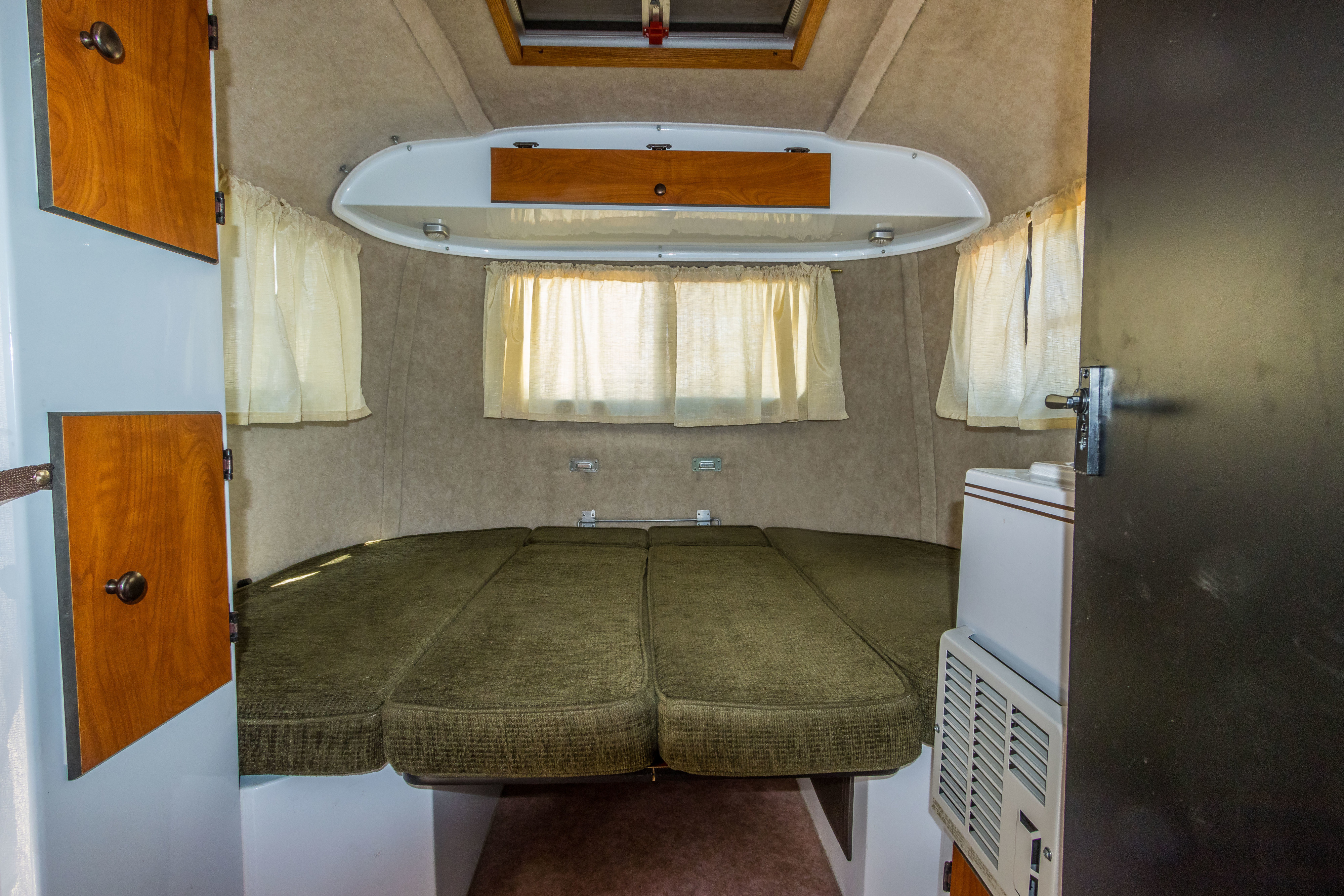 Inside a cozy RV rental: green cushioned bed/seating area, windows, cabinets, & AC unit.. Scamp Scamp Trailer 2015