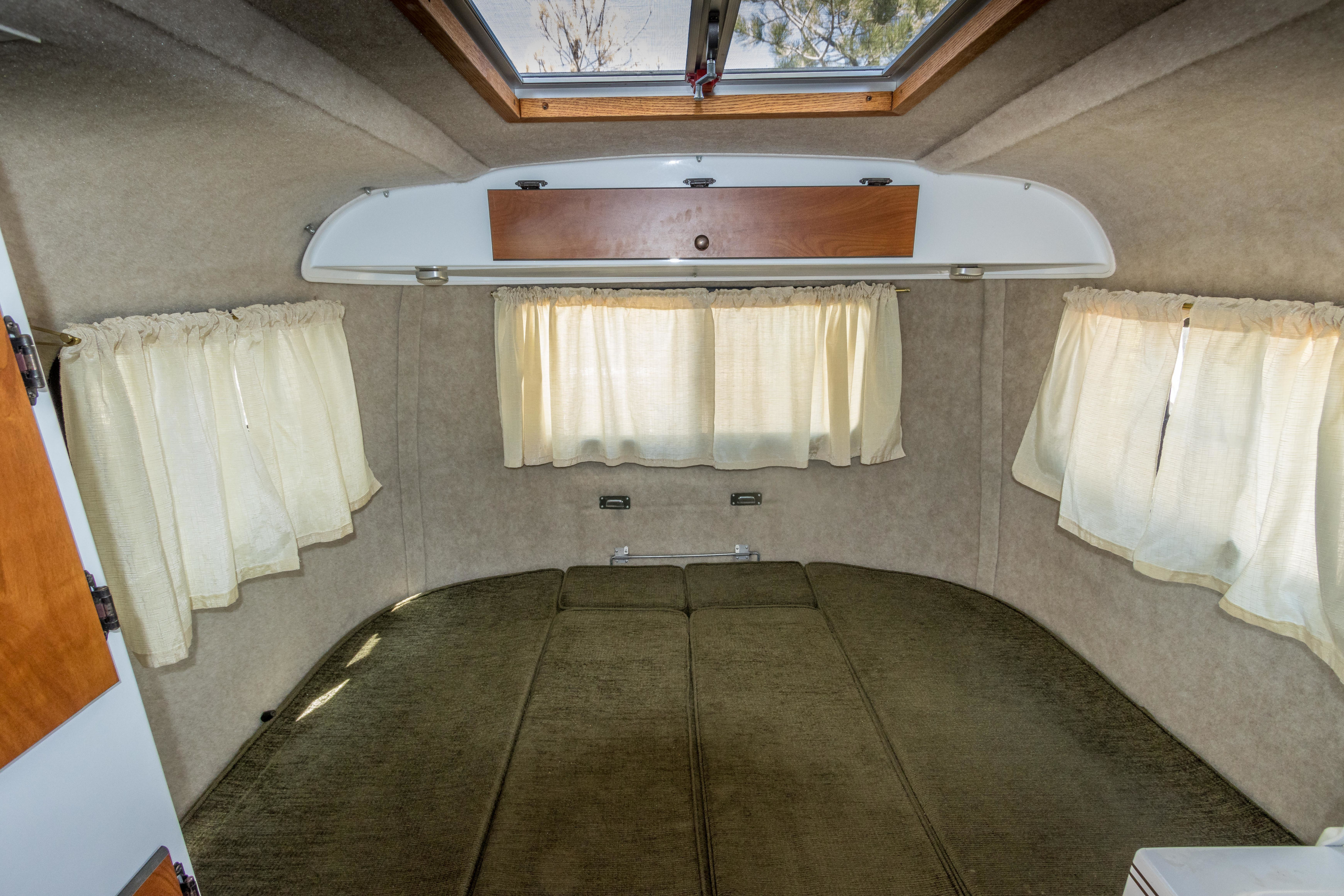 Cozy RV rental interior featuring a green bed, light curtains, overhead storage, and a skylight.. Scamp Scamp Trailer 2015