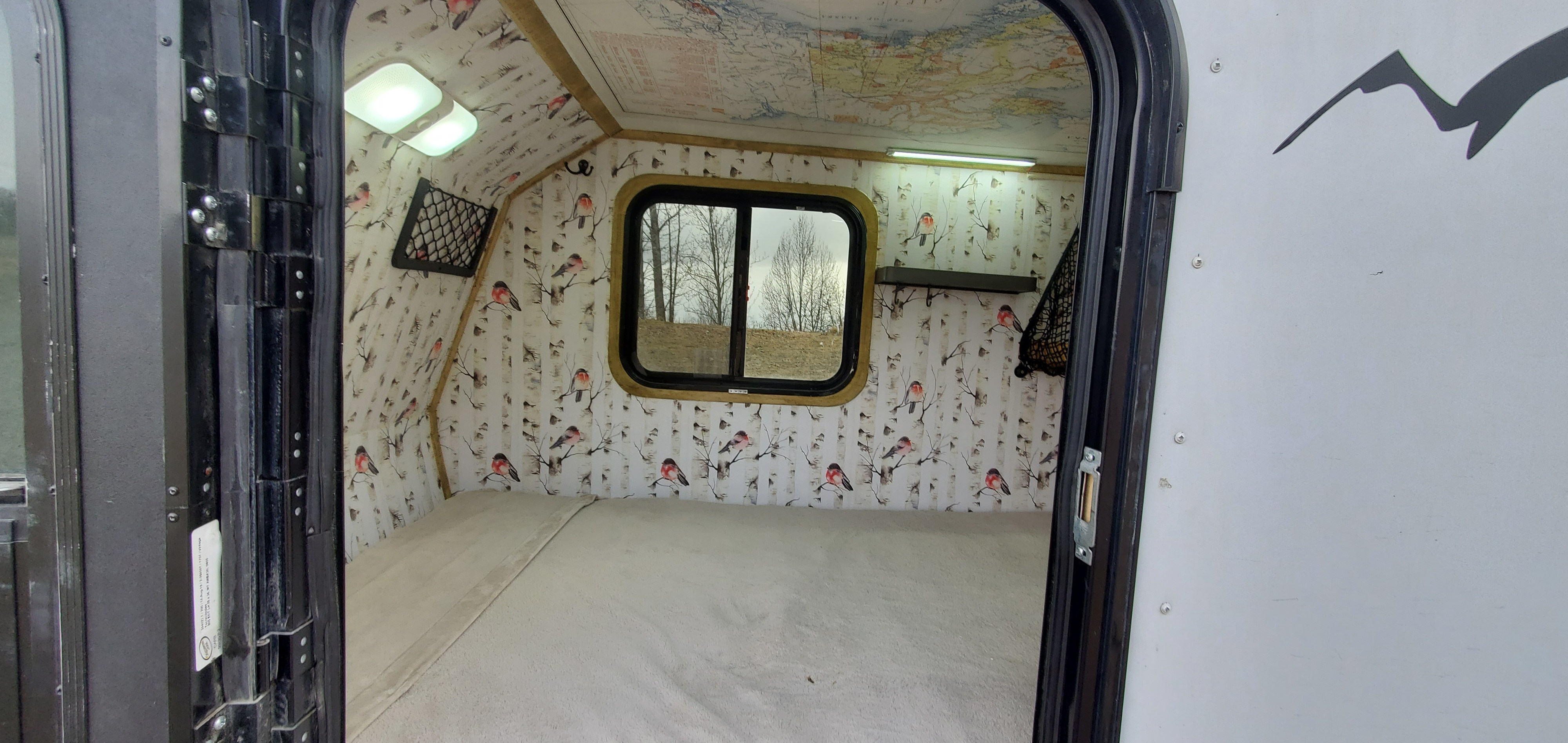 Explore this cozy RV rental interior: comfortable bed, unique bird & birch wall decor, map ceiling, and bright lighting.. Haulmark Homesteader 2005