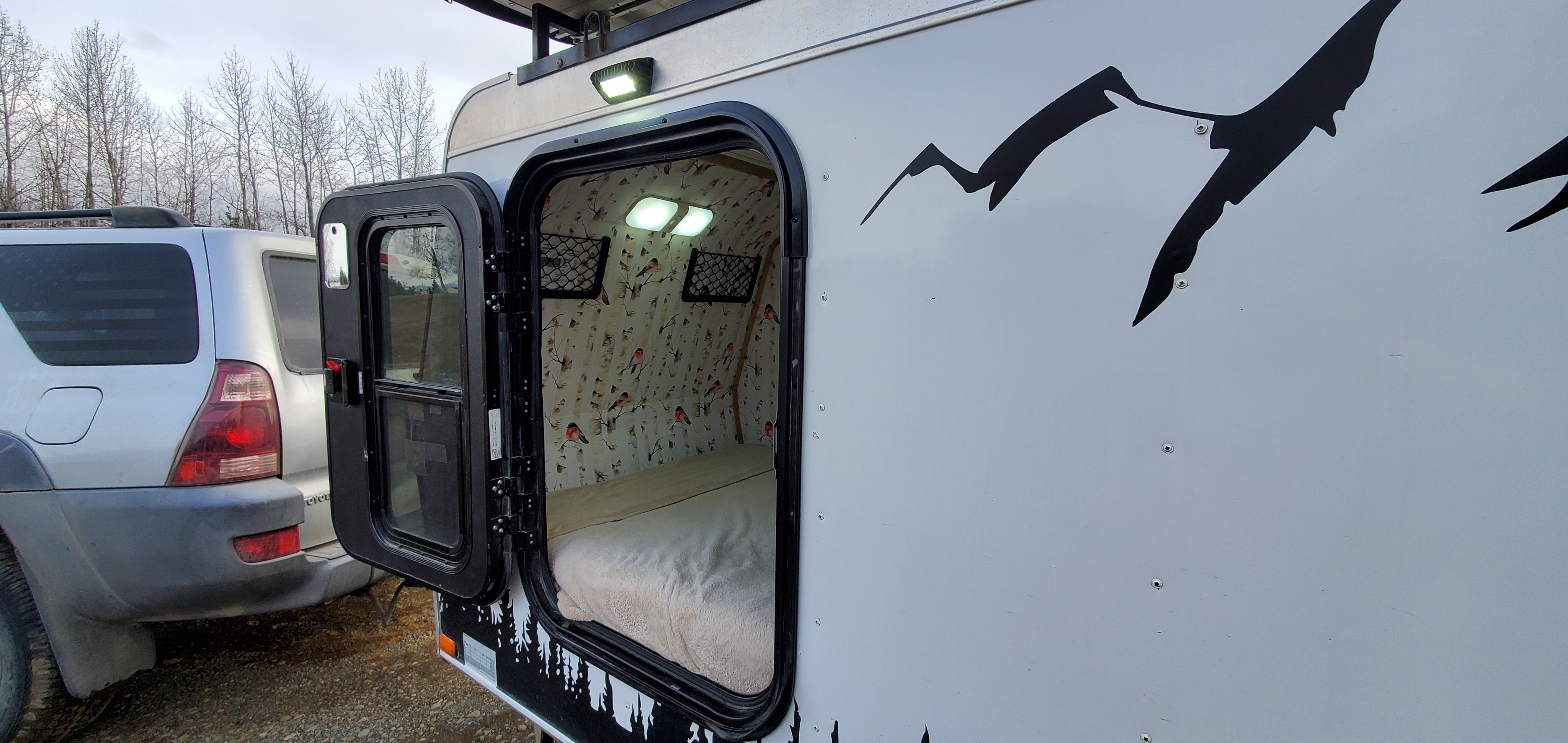 Cozy RV rental with open door revealing a bed, birch tree wallpaper, and lights inside. Ready for your next adventure.. Haulmark Homesteader 2005