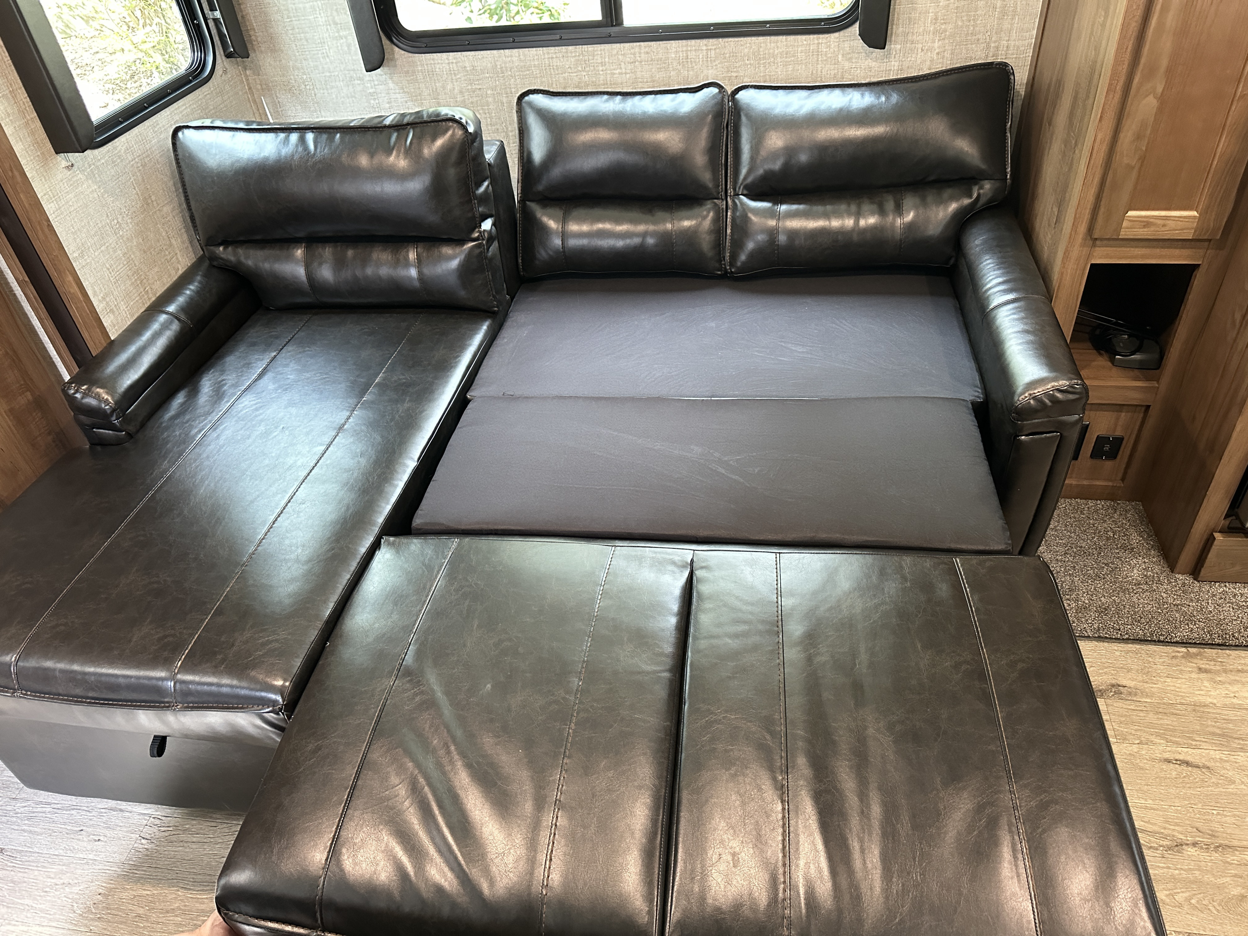 Flexible RV rental seating: A dark leather sofa extends to a bed, visible here mid-conversion.. Gulf Stream Envision 2020