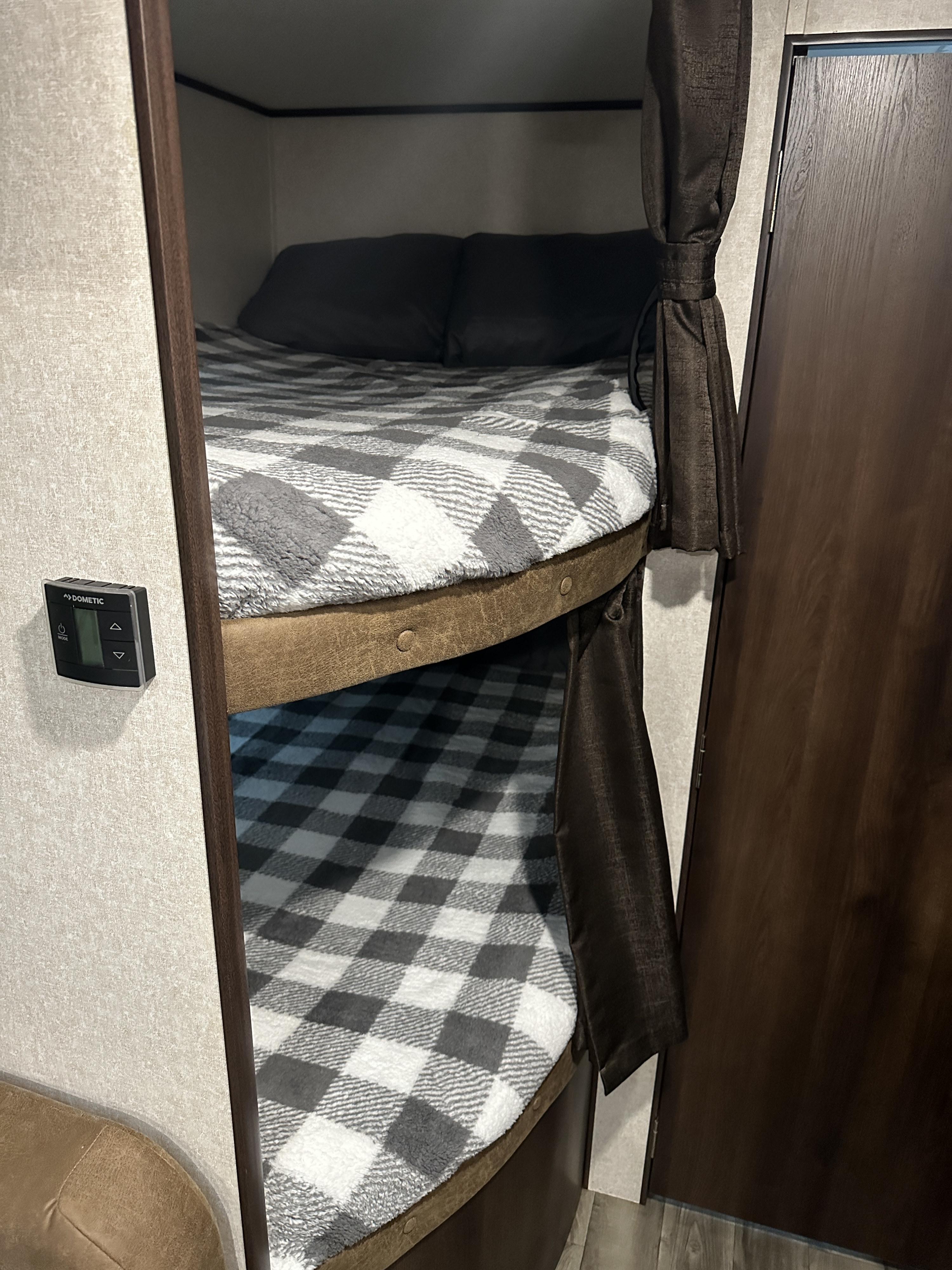 Inside an RV rental: comfortable bunk beds with plaid blankets. Features a Dometic control panel and dark curtains.. Jayco Jay Flight 2018