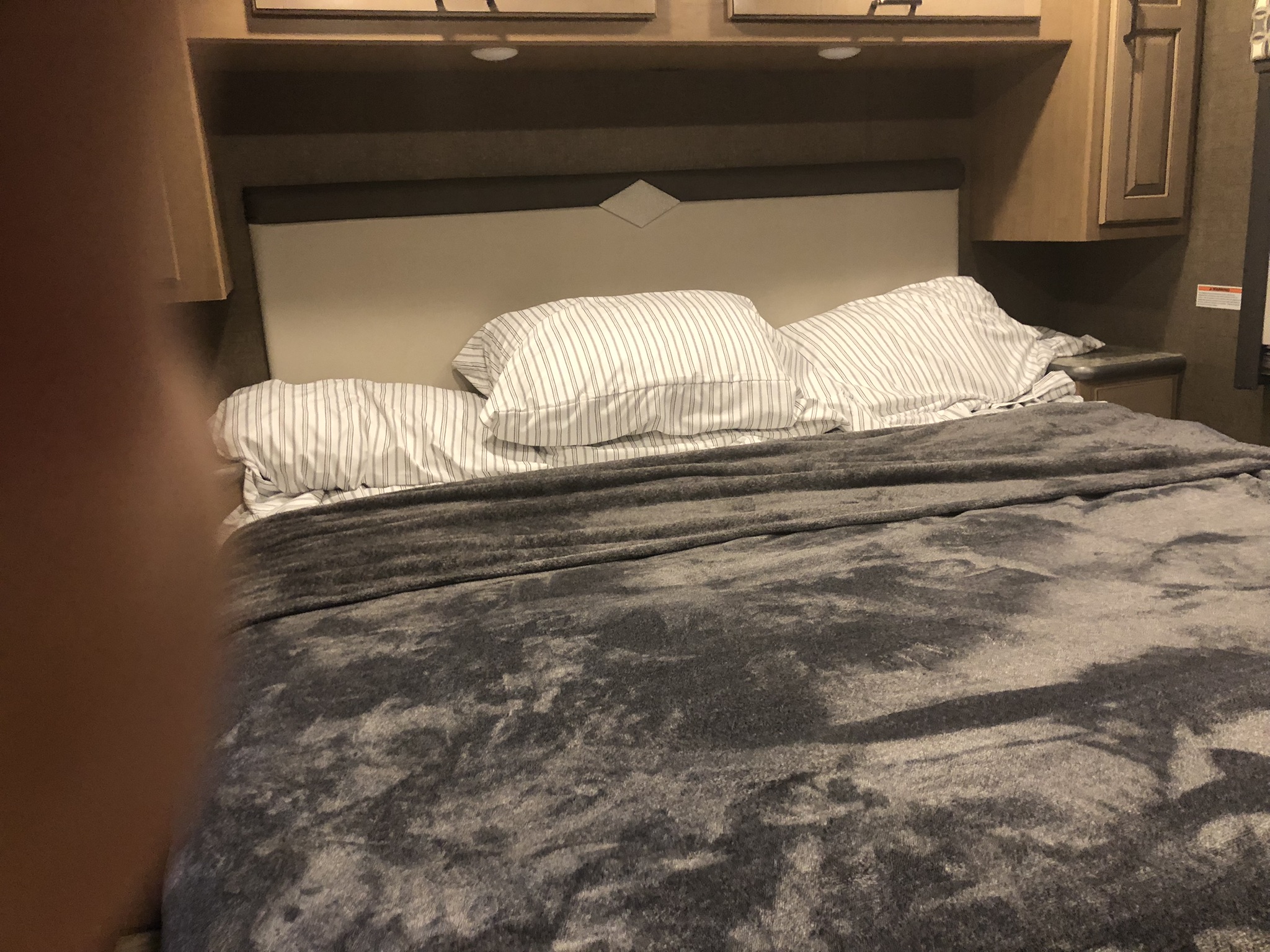 Comfortable RV rental bedroom featuring striped pillows, a cozy gray blanket, and practical overhead storage for travel.. Thor Hurricane 2020