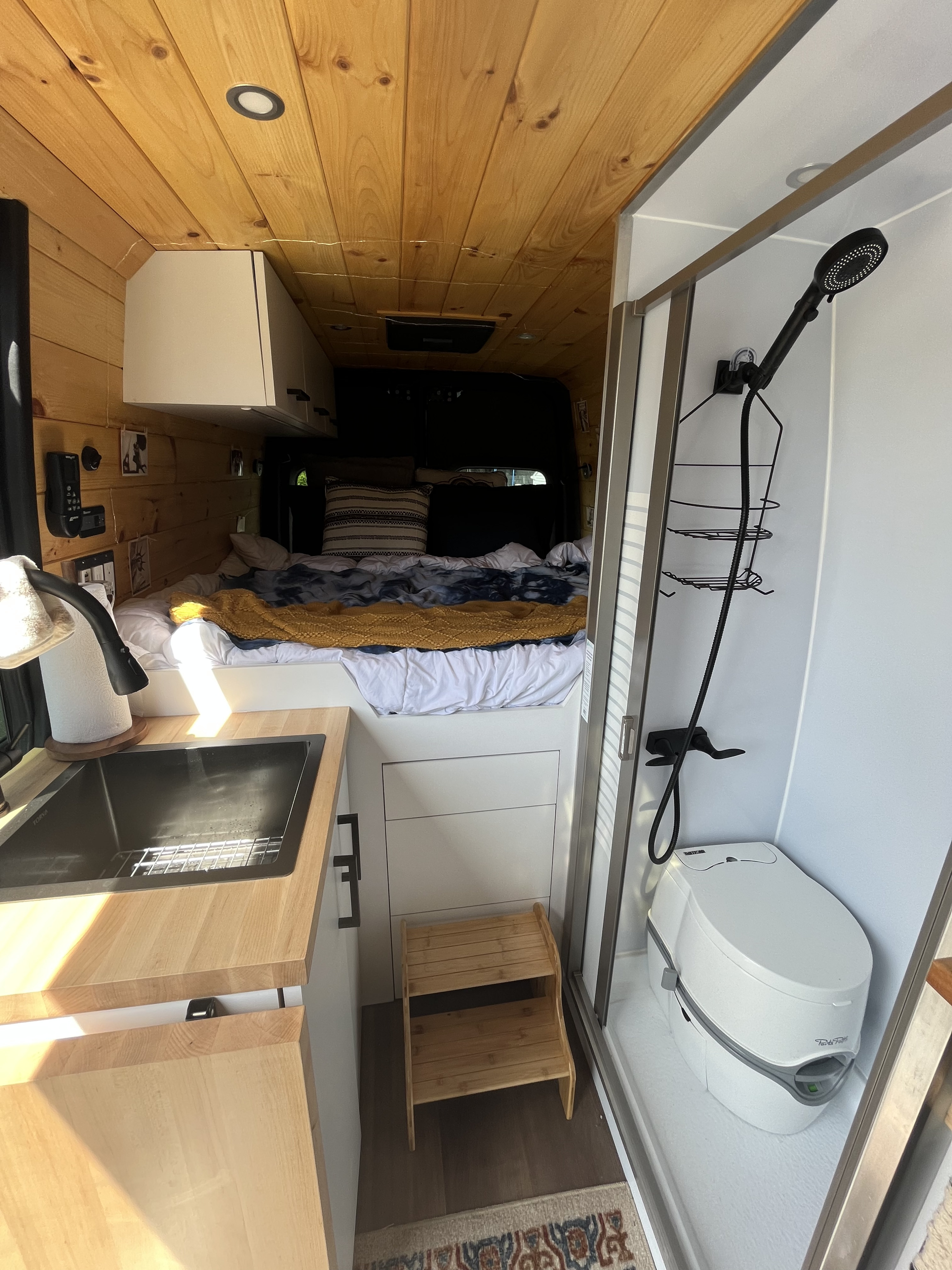 Cozy RV rental interior featuring a full bed, compact kitchen sink, and a shower/toilet combo for convenient mobile living.. Mercedes-Benz Sprinter 419 LWB High Roof 2019