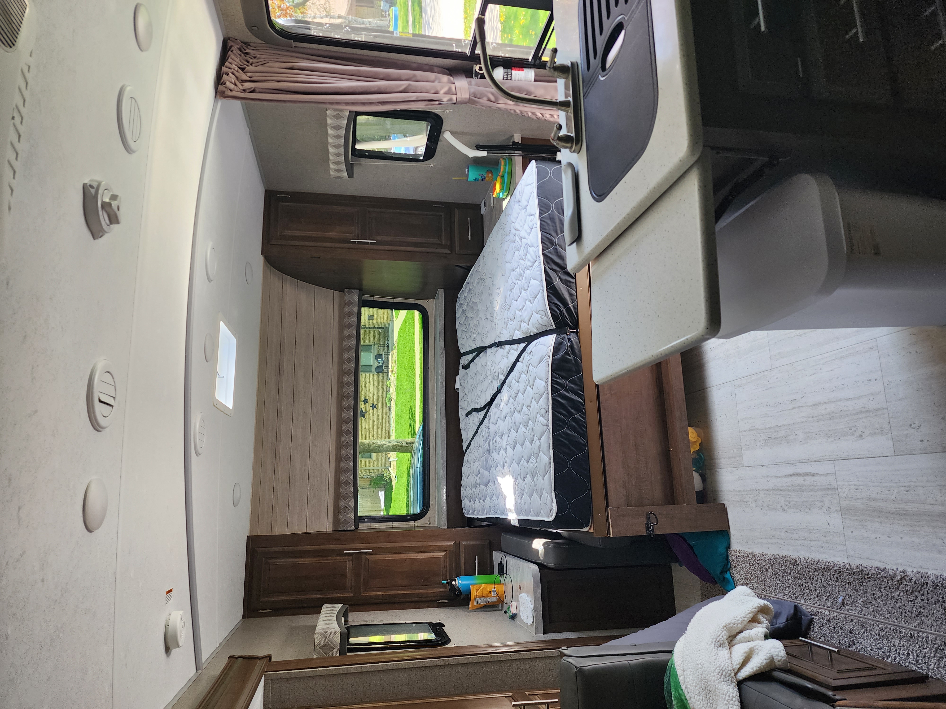 Inside an RV rental: a bedroom with a strapped mattress on the right, wooden cabinets, and part of the kitchen counter with a sink on the left.. Forest River Flagstaff Micro Lite 2020
