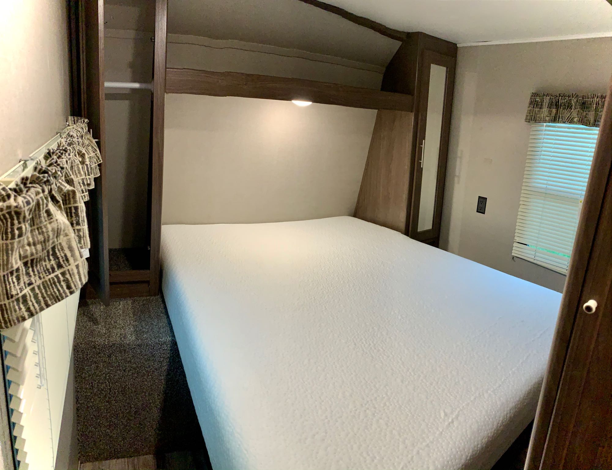Cozy RV rental bedroom featuring a clean white bed, built-in storage, and a bright window with blinds.. Keystone RV Hideout LHS 2019