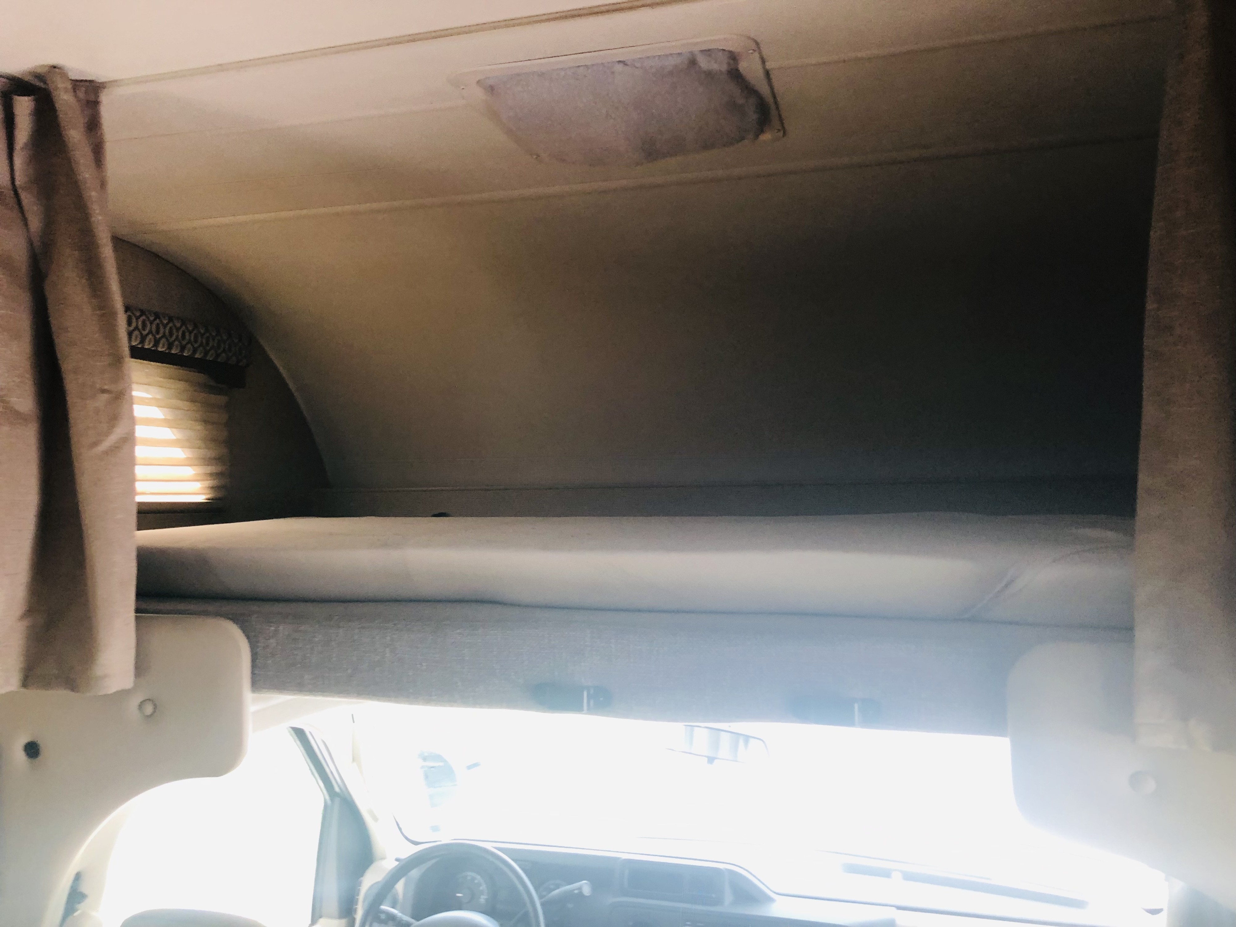 Inside an RV rental, showing the cozy over-cab bunk, privacy curtains, and bright dashboard area.. Thor Freedom Elite 2019